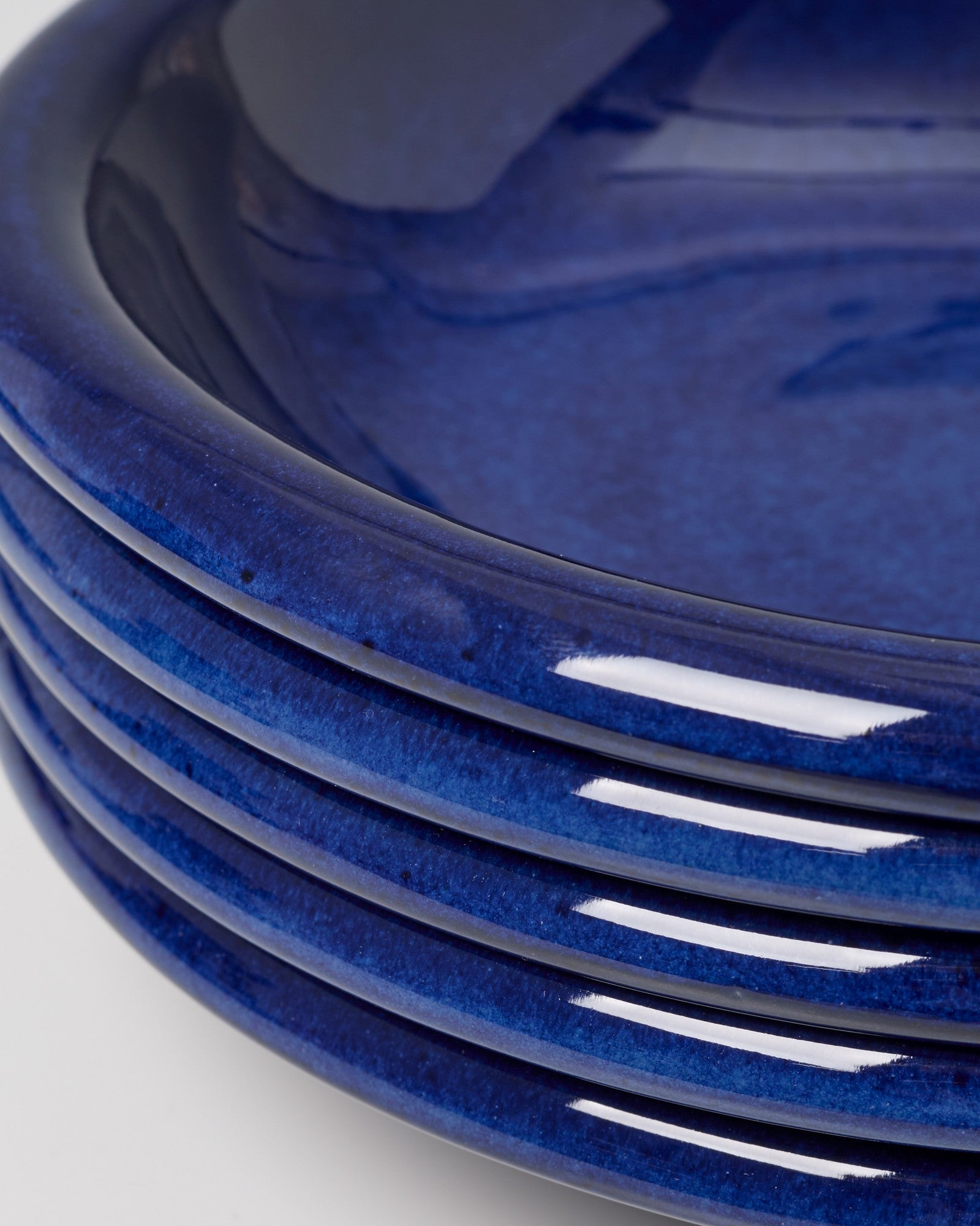 Ein Stapel von fünf glänzend blauen Keramiktellern vor einem neutralen Hintergrund.