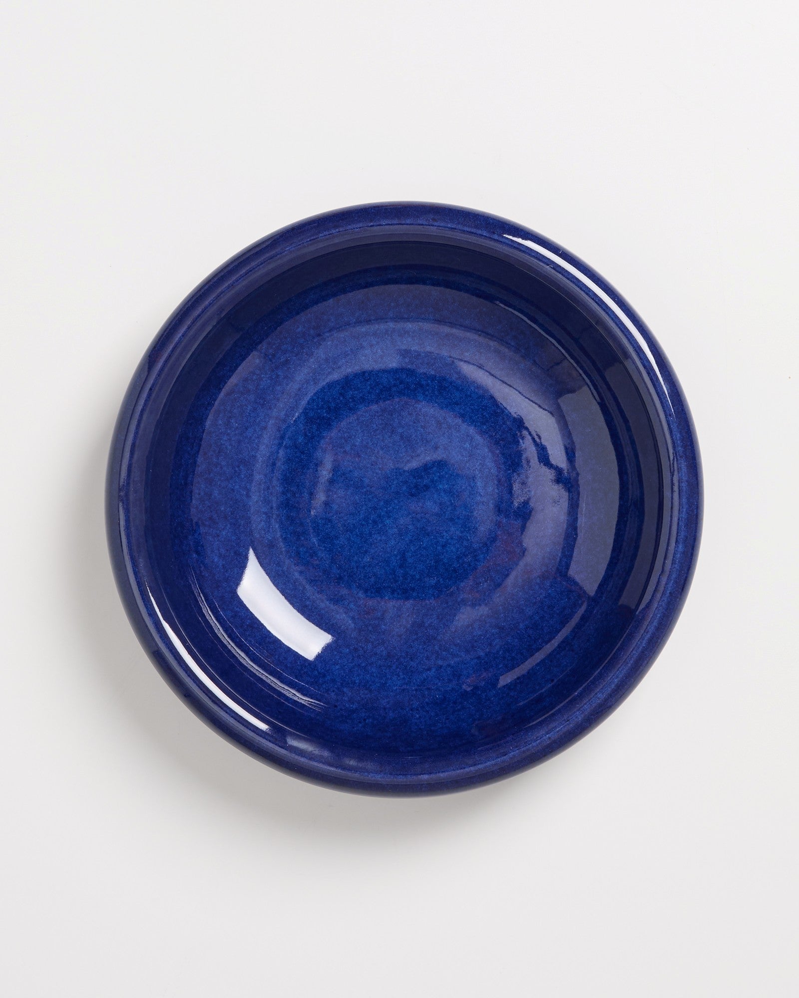 Dunkelblauer, glänzender Keramikteller auf weißem Hintergrund fotografiert.