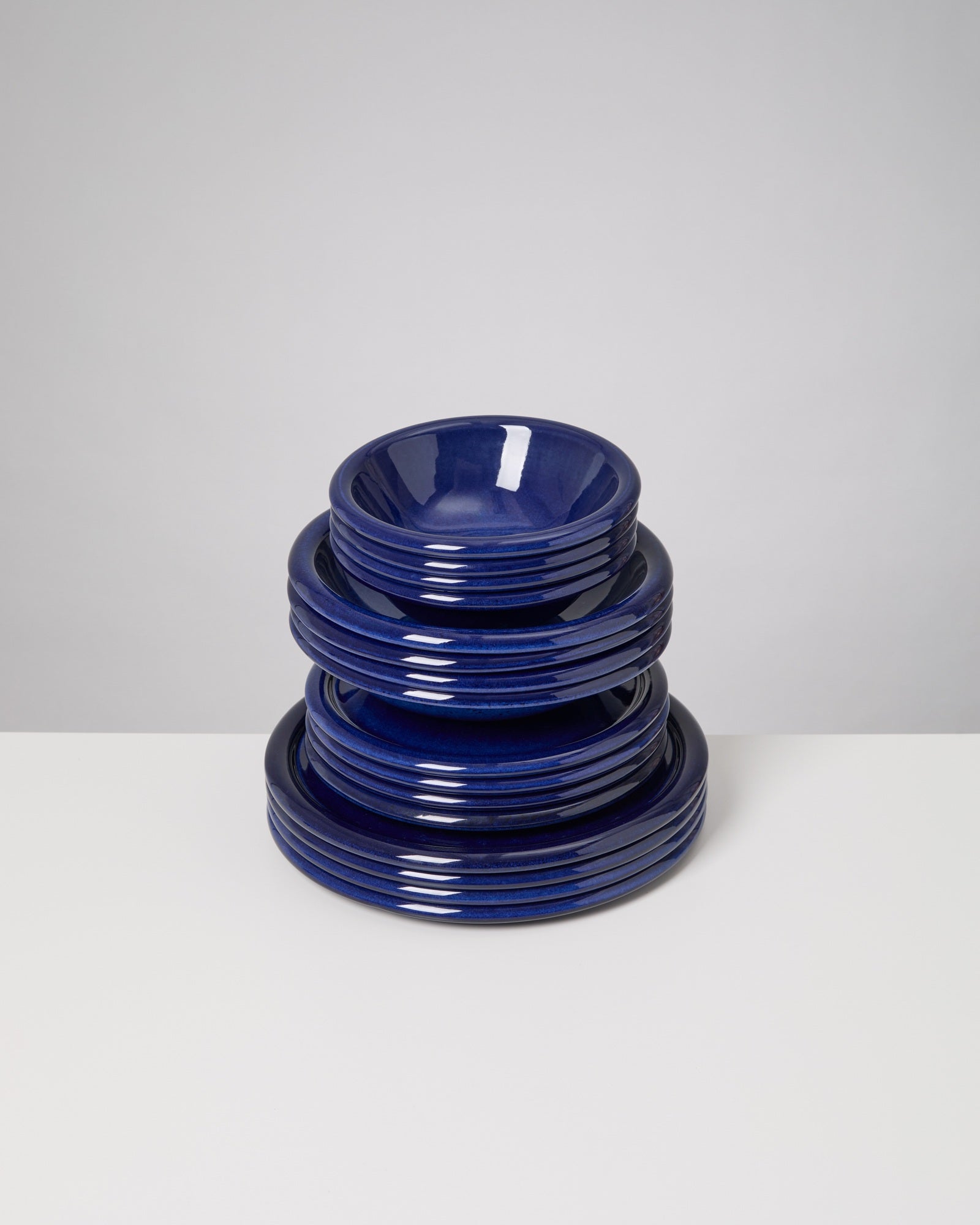 Ein Stapel dunkelblauer Keramikteller steht auf einem weißen Tisch vor einem grauen Hintergrund.