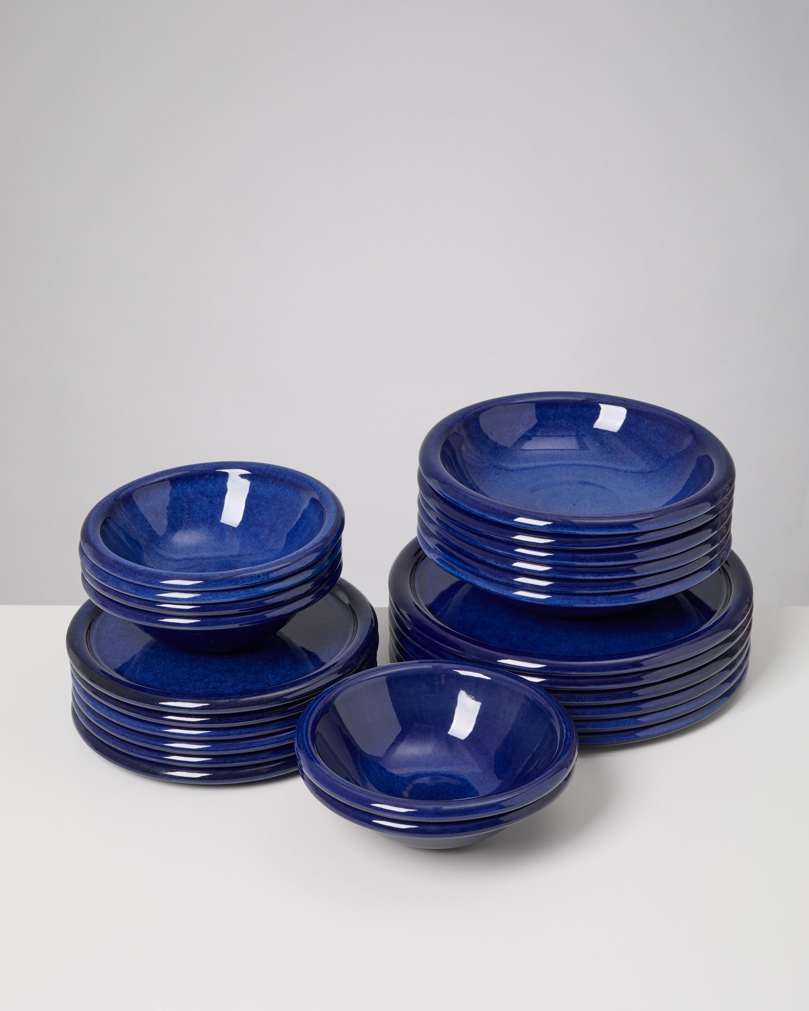 Stapel aus blauen Keramiktellern und Schüsseln auf einem weißen Tisch.