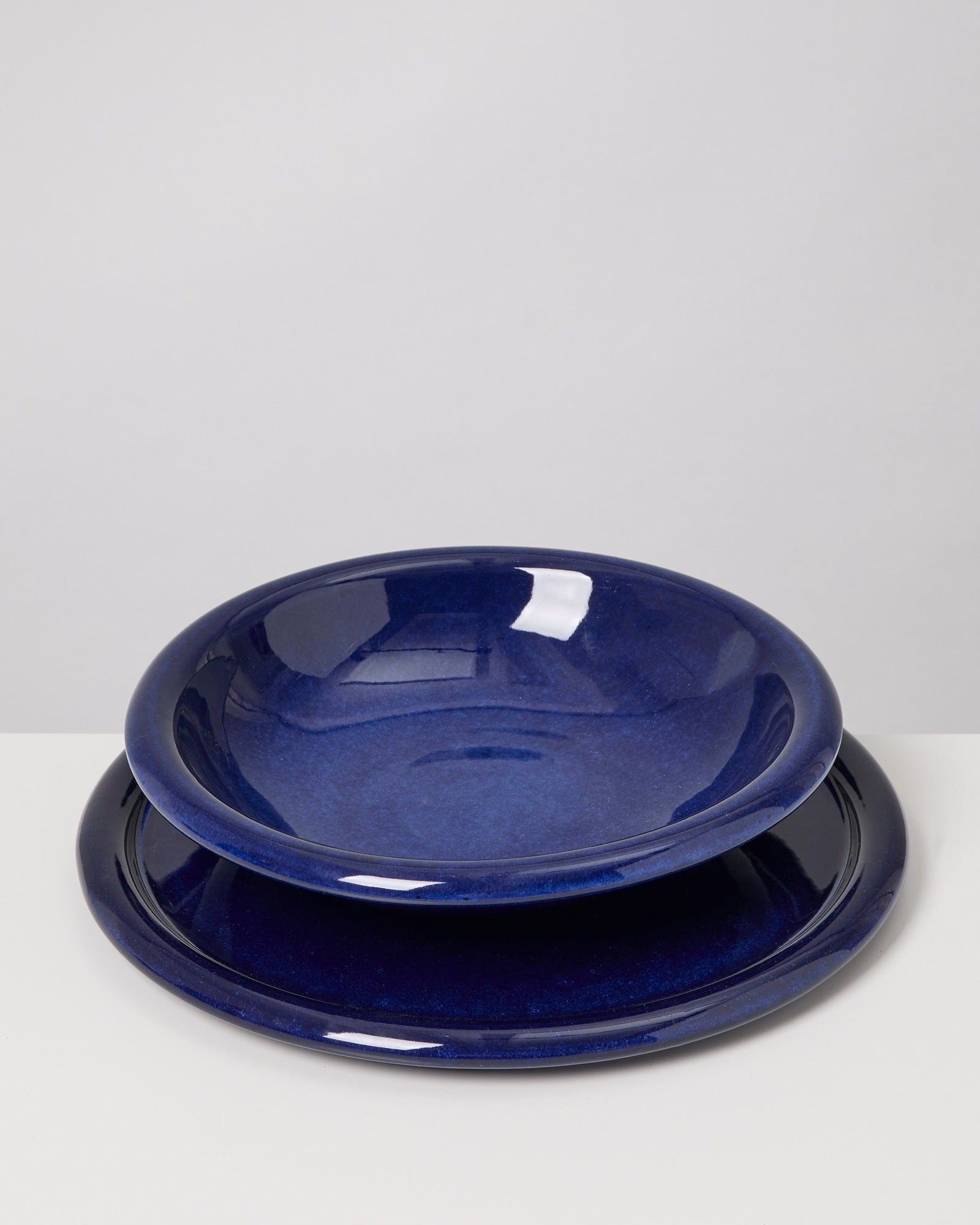 Zwei dunkelblaue Keramikteller auf einem hellen Tisch, einer ist leicht in den anderen gestellt.