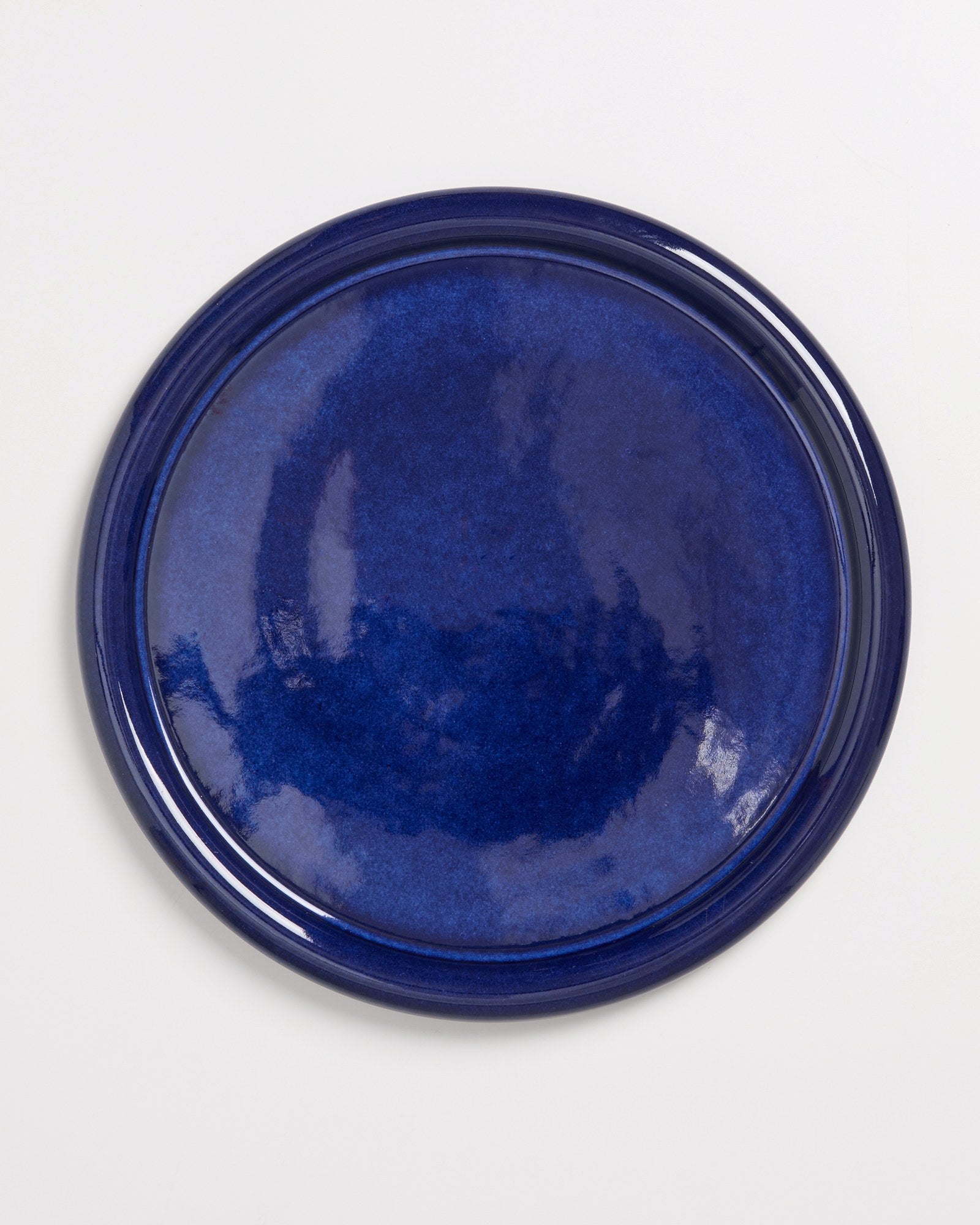 Dunkelblauer, runder Keramikteller auf weißem Hintergrund.