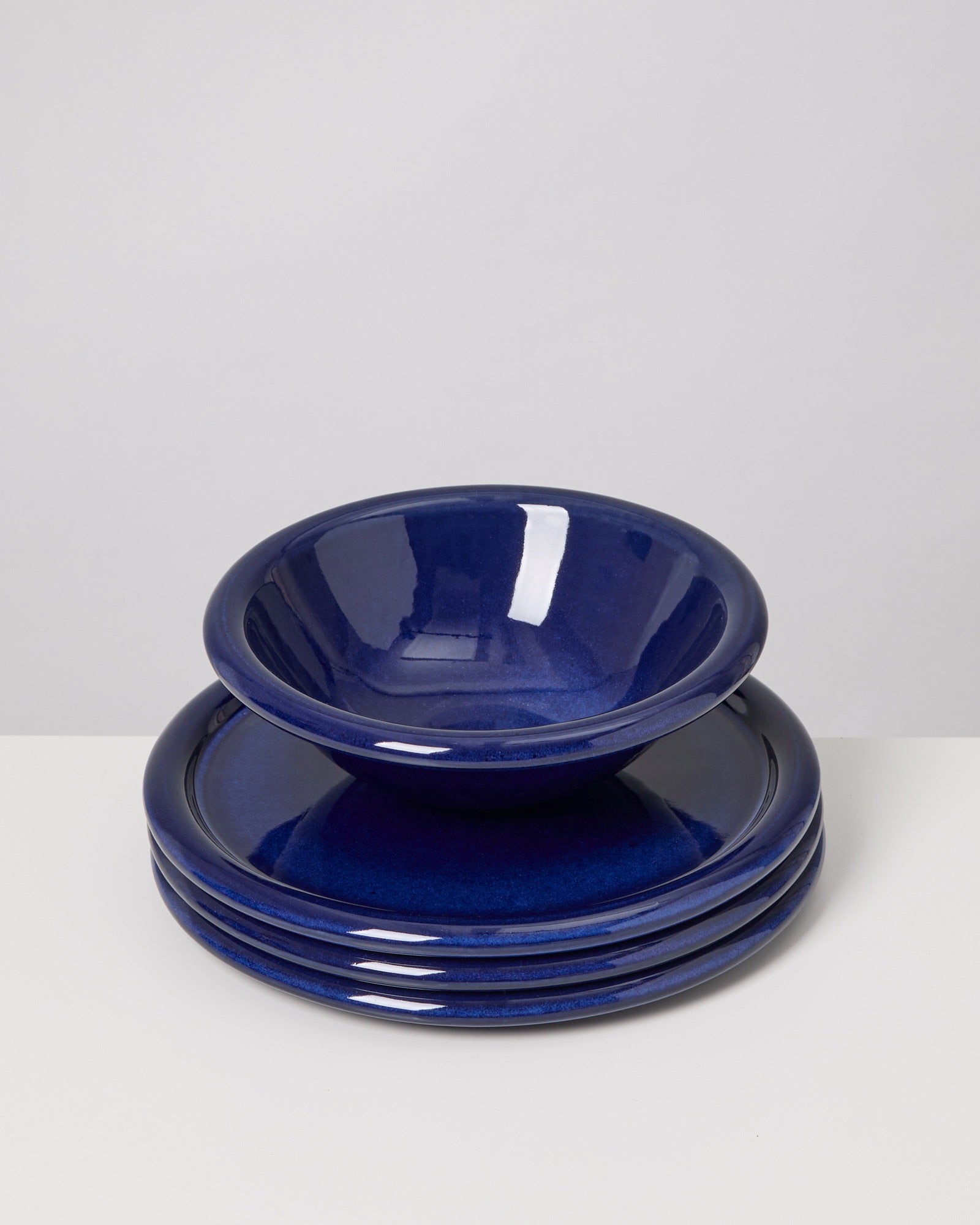 Vier blaue Keramikteller und eine passende Schüssel auf einem weißen Untergrund gestapelt.