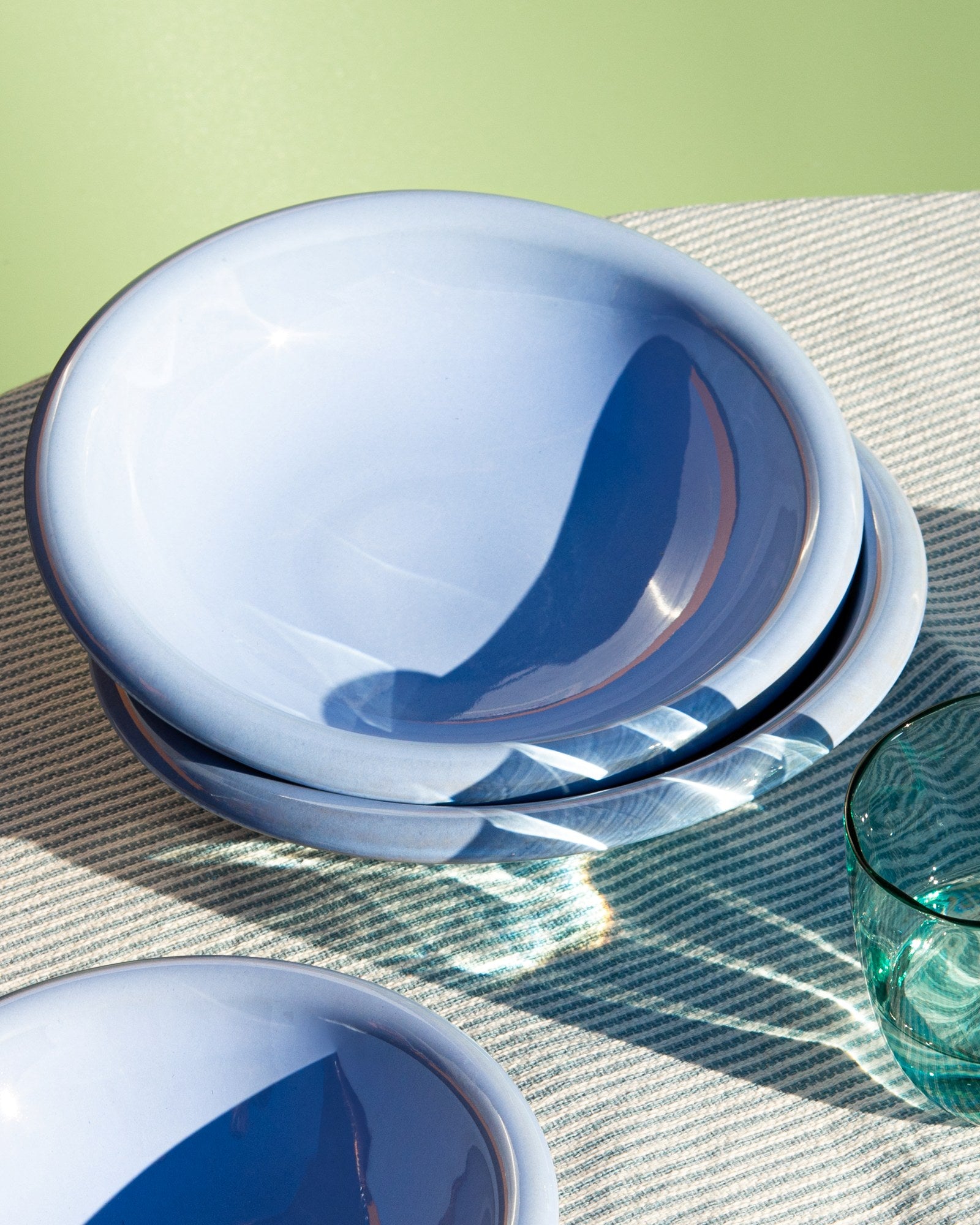 Blaues Geschirr und ein grünes Glas auf einer gestreiften Tischdecke vor grünem Hintergrund.