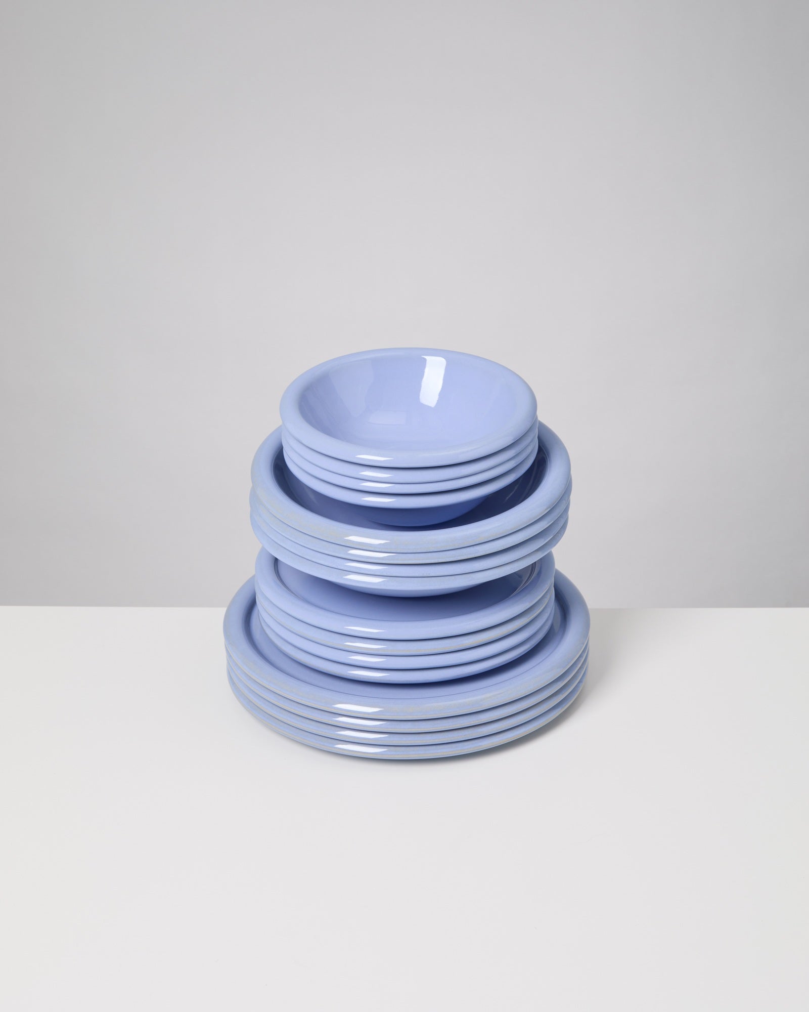 Ein Stapel hellblauer Teller und Schüsseln auf einem weißen Tisch vor einem grauen Hintergrund.
