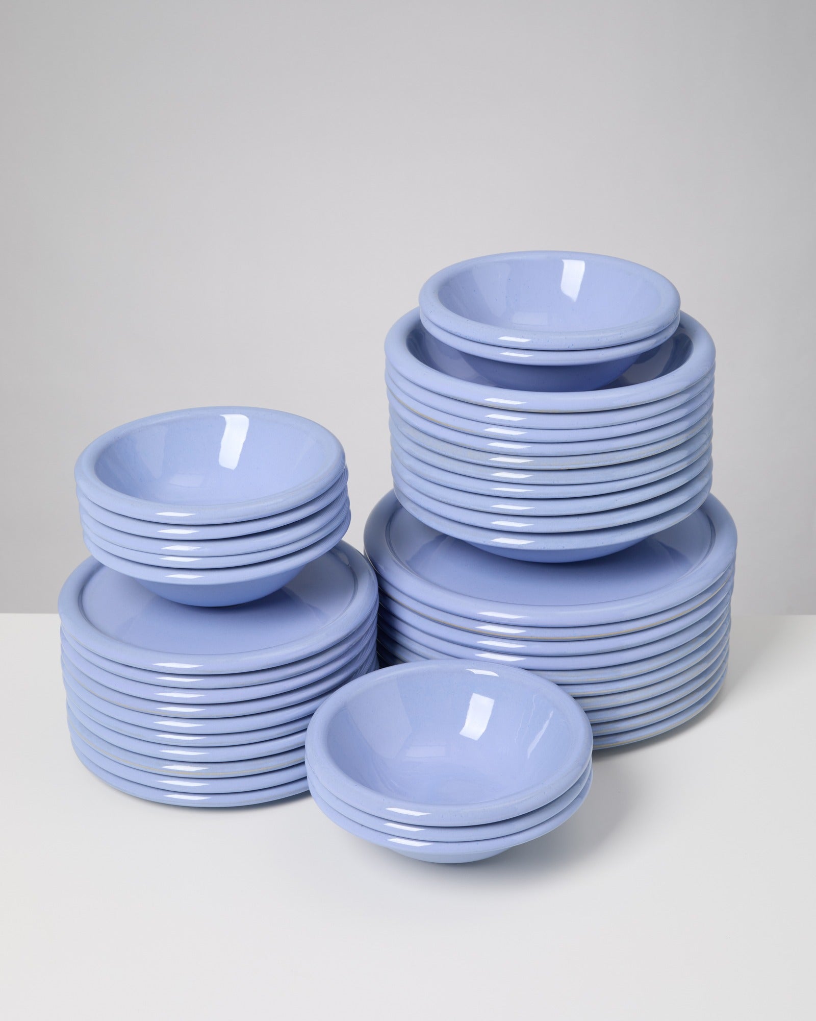 Stapel hellblauer, glänzender Teller und Schalen auf weißem Hintergrund.