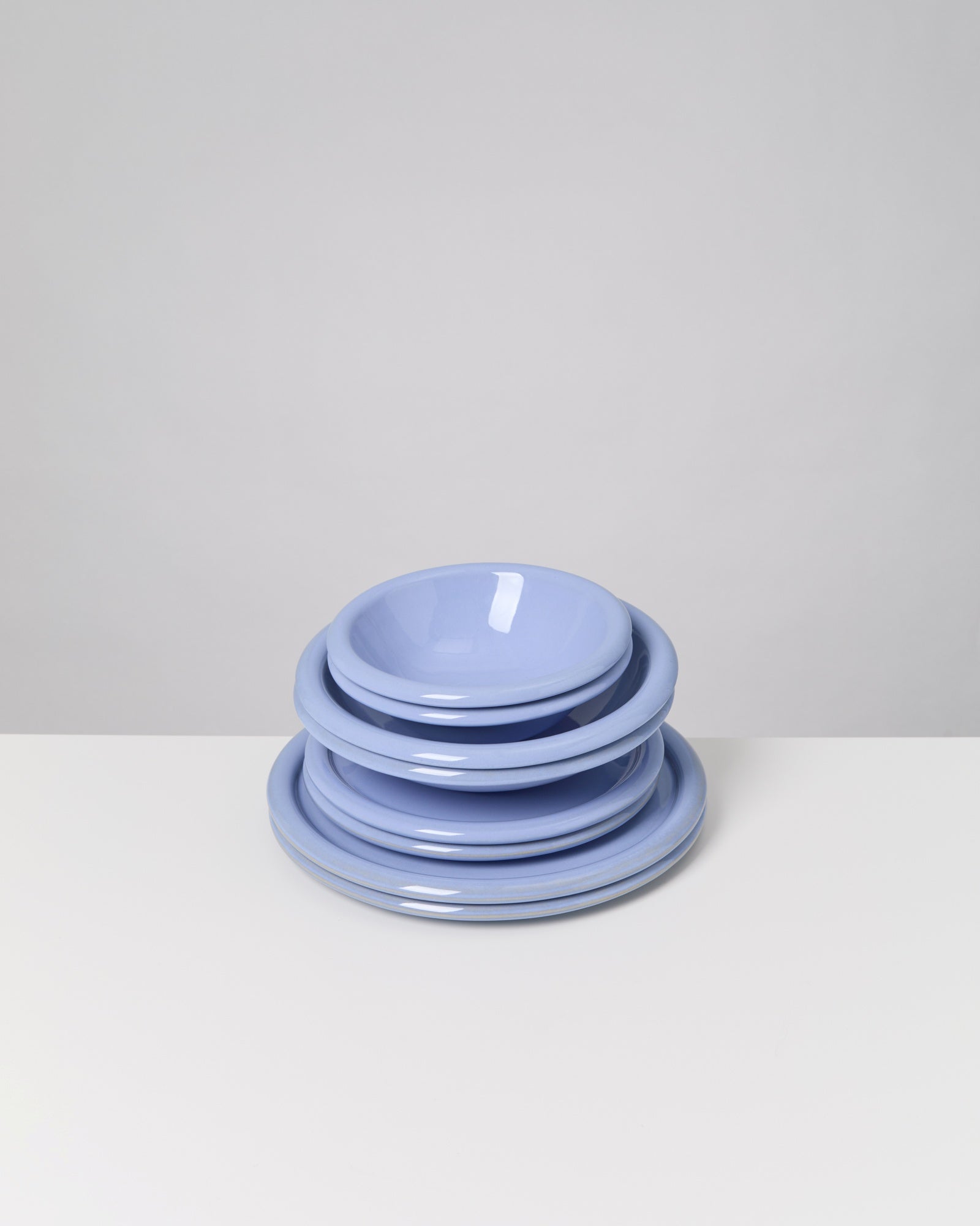 Ein Stapel aus fünf lavendelblauen Tellern auf einer weißen Oberfläche vor einem grauen Hintergrund.