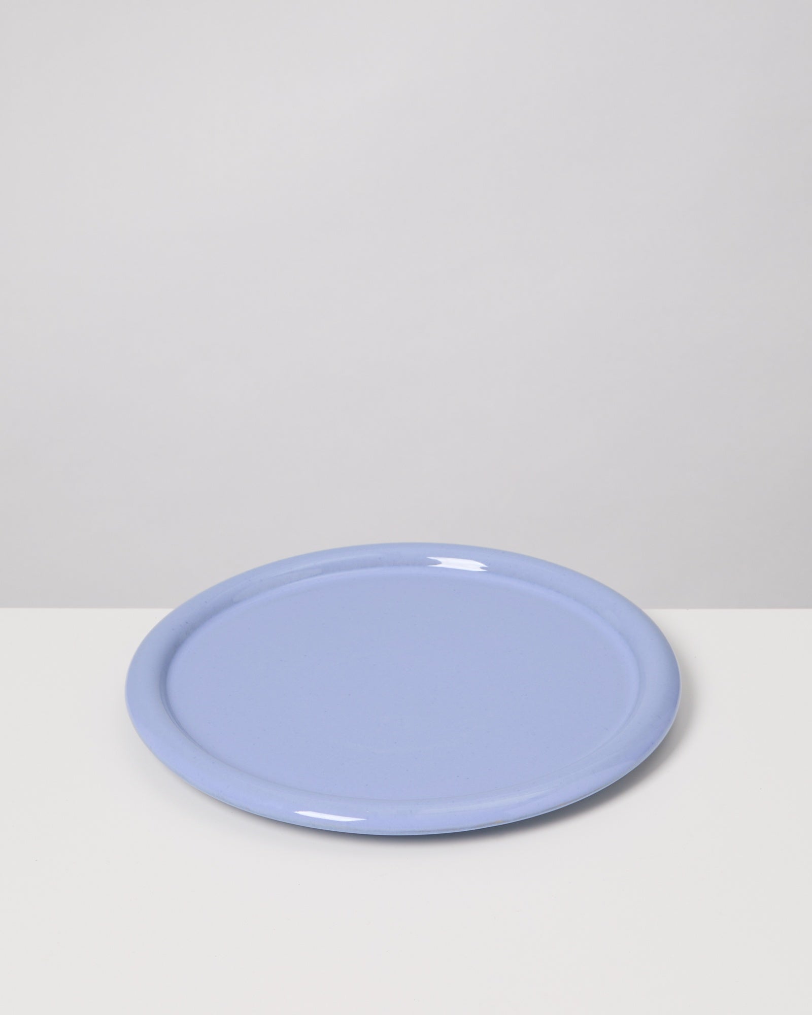 Ein hellblauer Teller liegt auf einer weißen Oberfläche vor einem grauen Hintergrund.