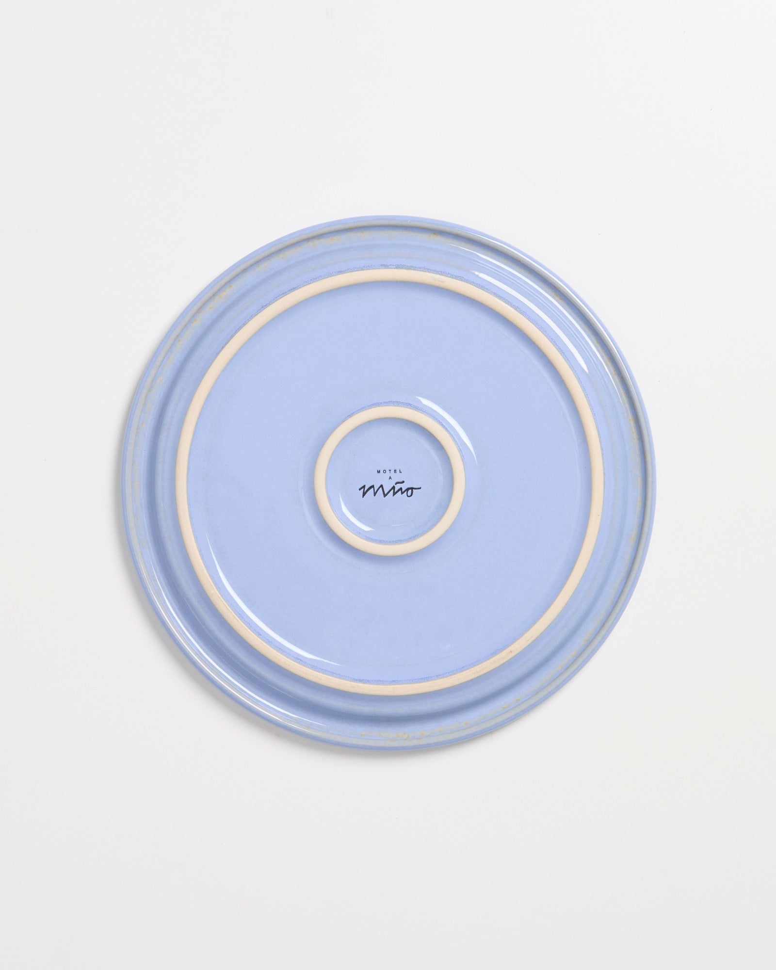 Blauer Keramikteller mit beigem Rand und schwarzem Schriftzug in der Mitte auf einer weißen Oberfläche.