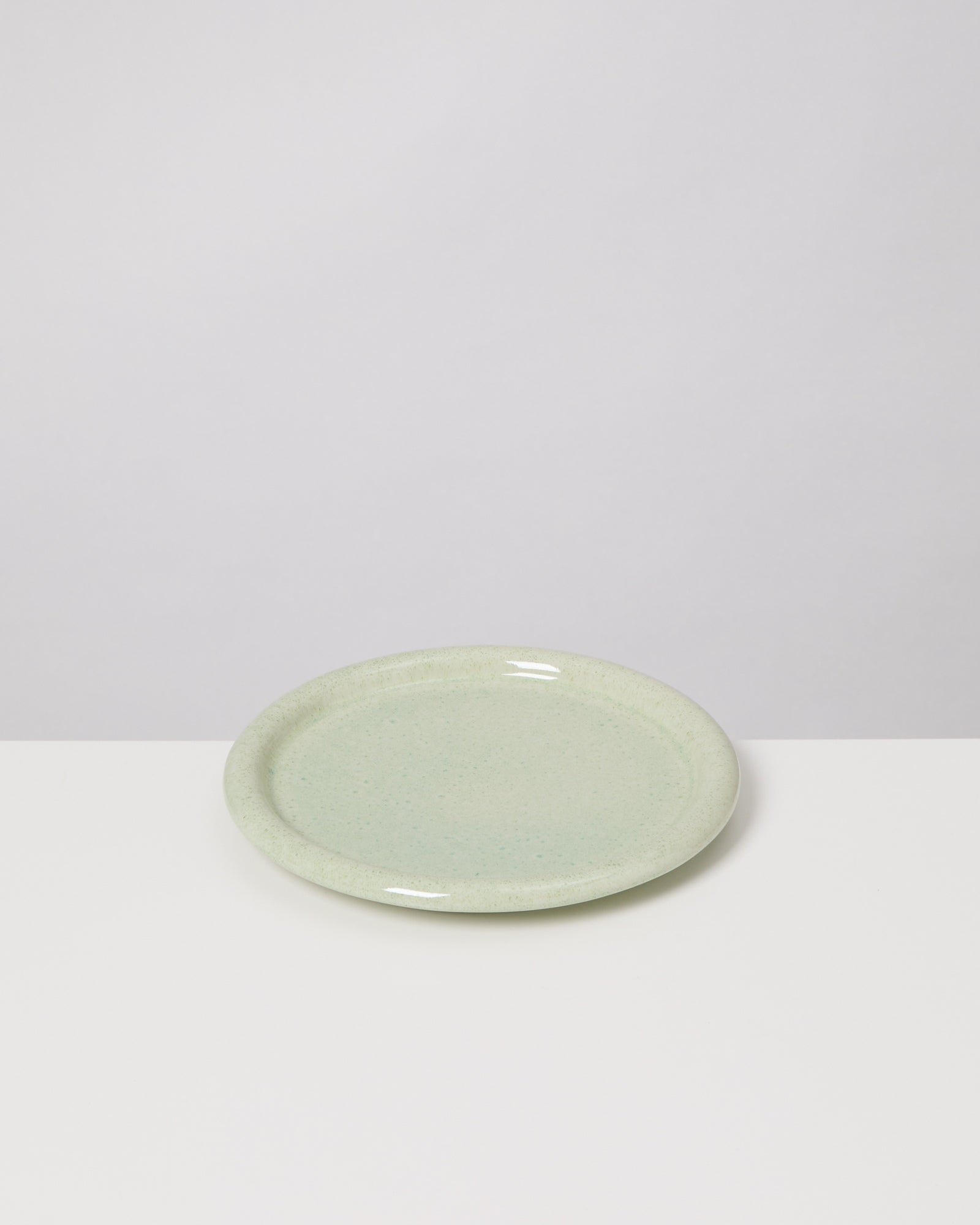 Hellgrüner Keramikteller auf einem weißen Tisch vor grauem Hintergrund.