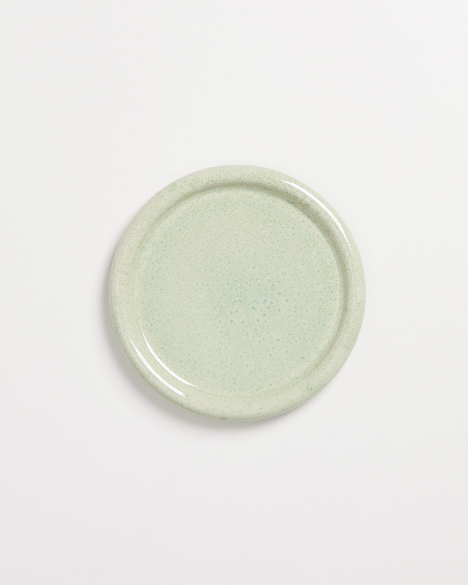 Runder, hellgrüner Keramikteller mit einem gesprenkelten Muster auf weißem Hintergrund.