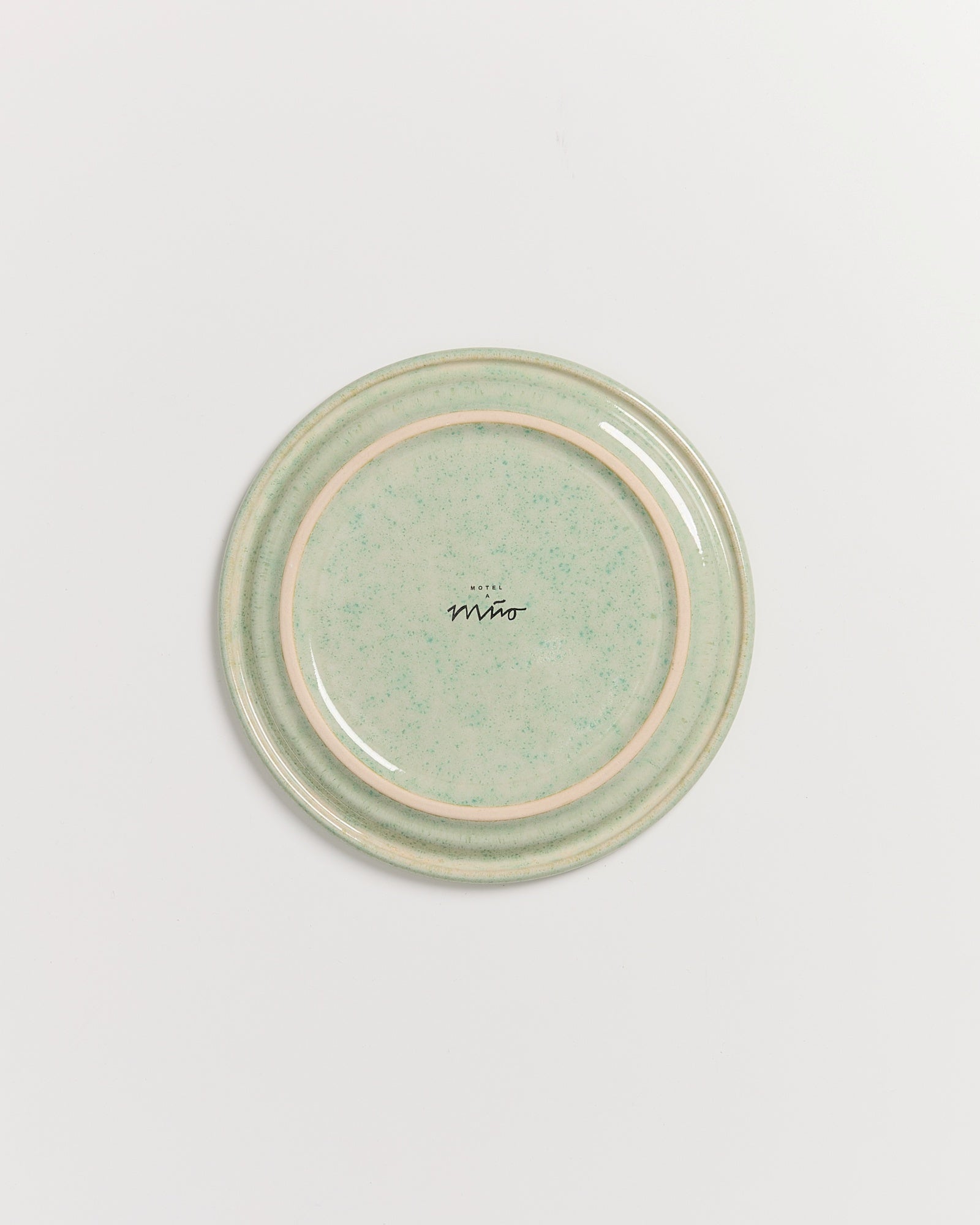 Grüner Keramikteller mit Schriftzug "Motel Miō" in der Mitte und gesprenkeltem Muster auf hellem Hintergrund.
