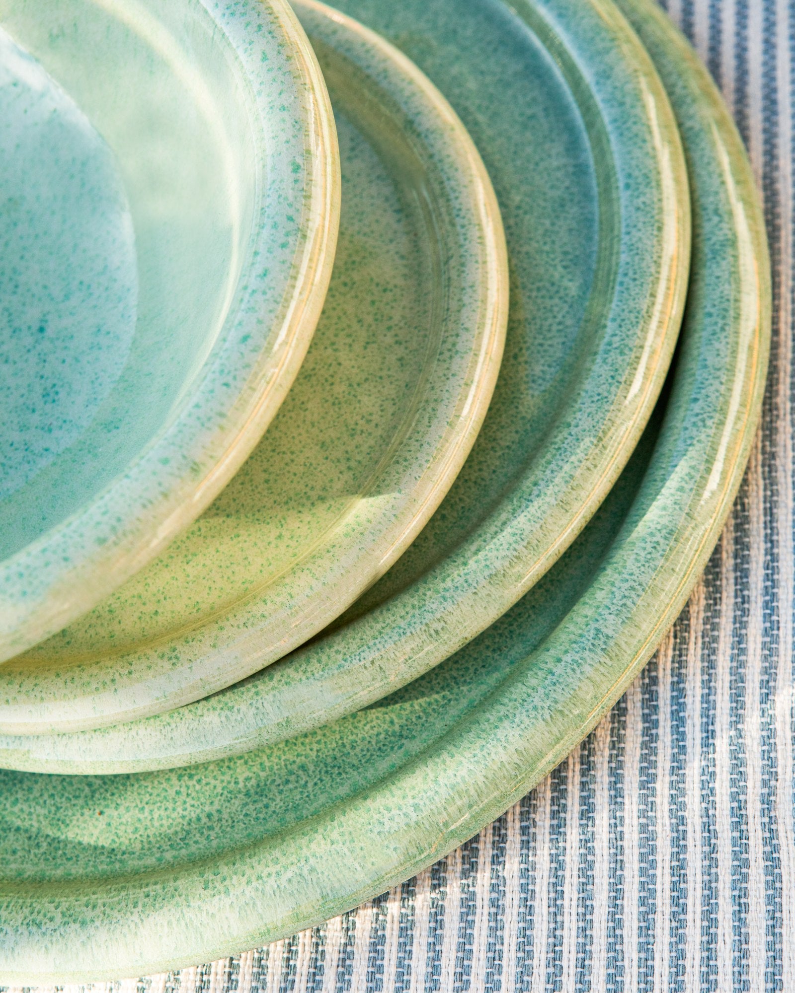 Verschachtelte grüne Keramikteller mit gesprenkeltem Muster, liegend auf einem gestreiften Tuch.