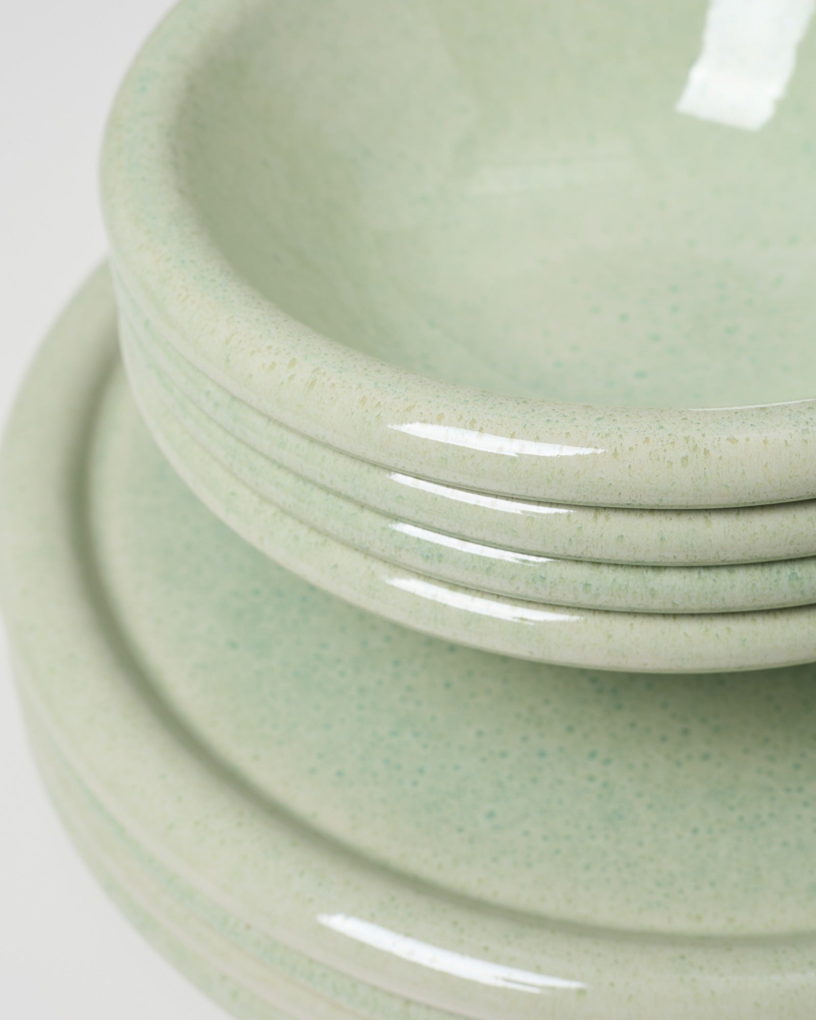 Stapel von türkisfarbenen Keramikschalen und Tellern mit glänzender Oberfläche, nah aufgenommen.