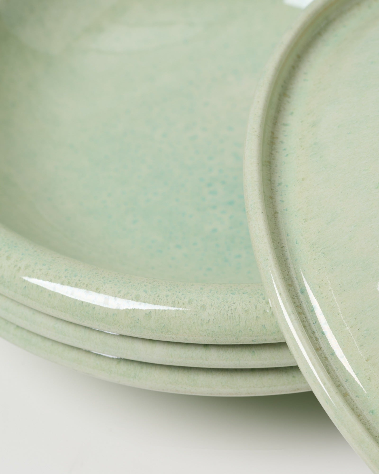 Nahaufnahme von mehreren übereinander gestapelten, hellgrünen Keramiktellern mit glatter, glänzender Oberfläche.