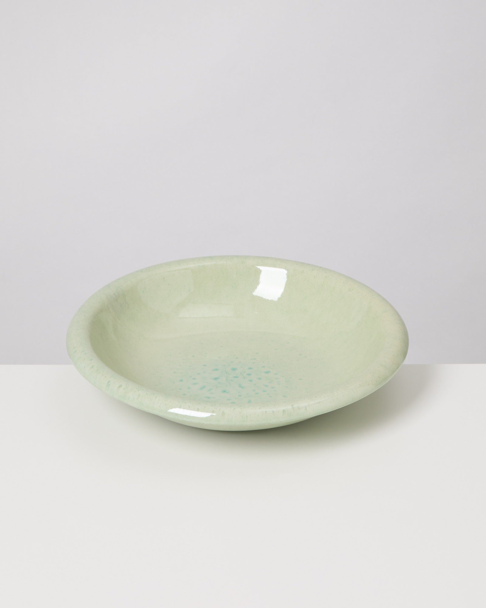 Hellgrüne Keramikschale mit glänzender Oberfläche auf einem weißen Hintergrund.