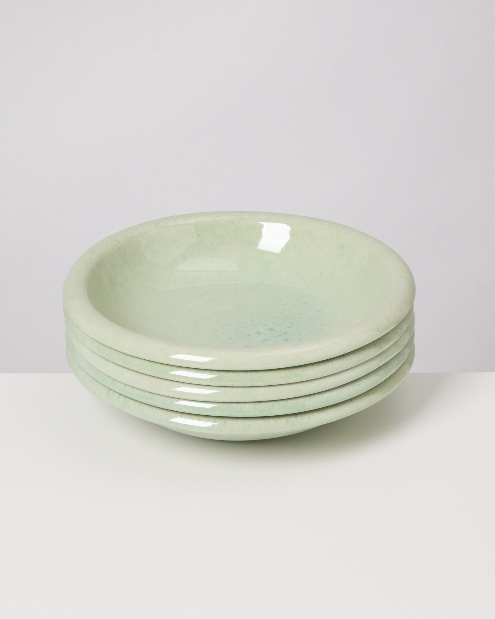 Fünf grüne, gestapelte Keramikteller auf einem weißen Hintergrund.