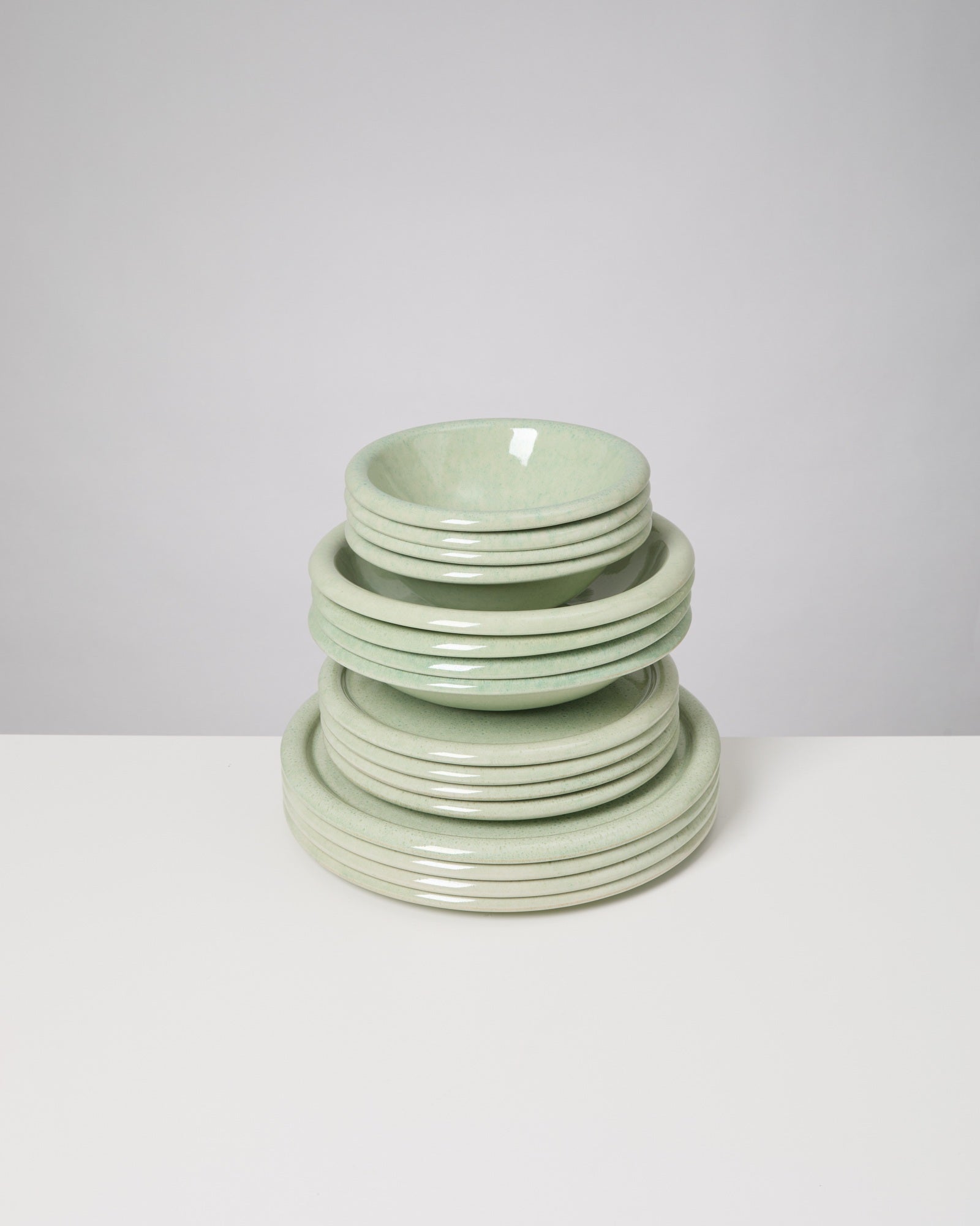 Ein Stapel grüner Keramikteller und -schüsseln auf einem weißen Tisch.