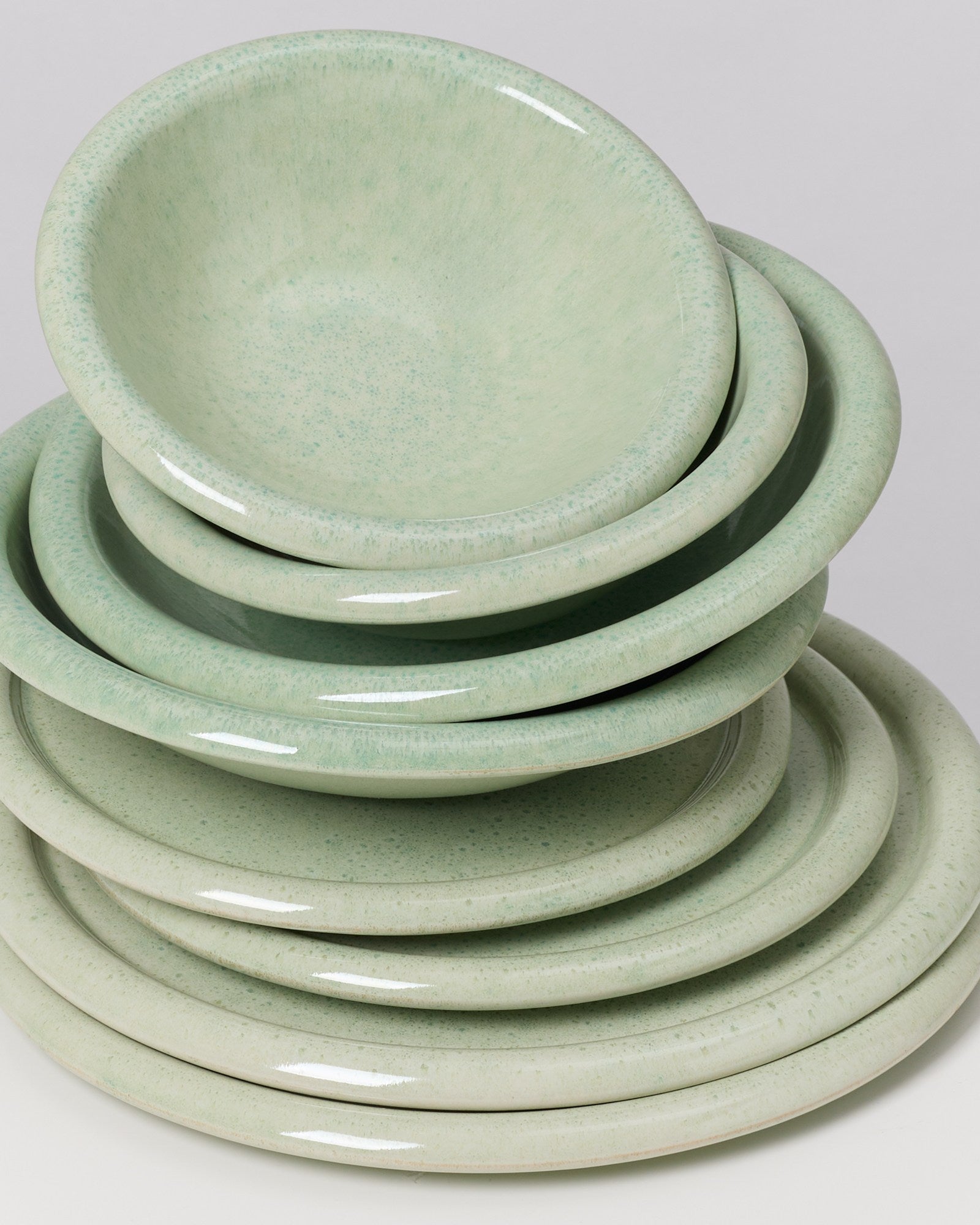 Ein Stapel aus acht grünen, matten Keramikschüsseln und -tellern auf weißem Hintergrund.