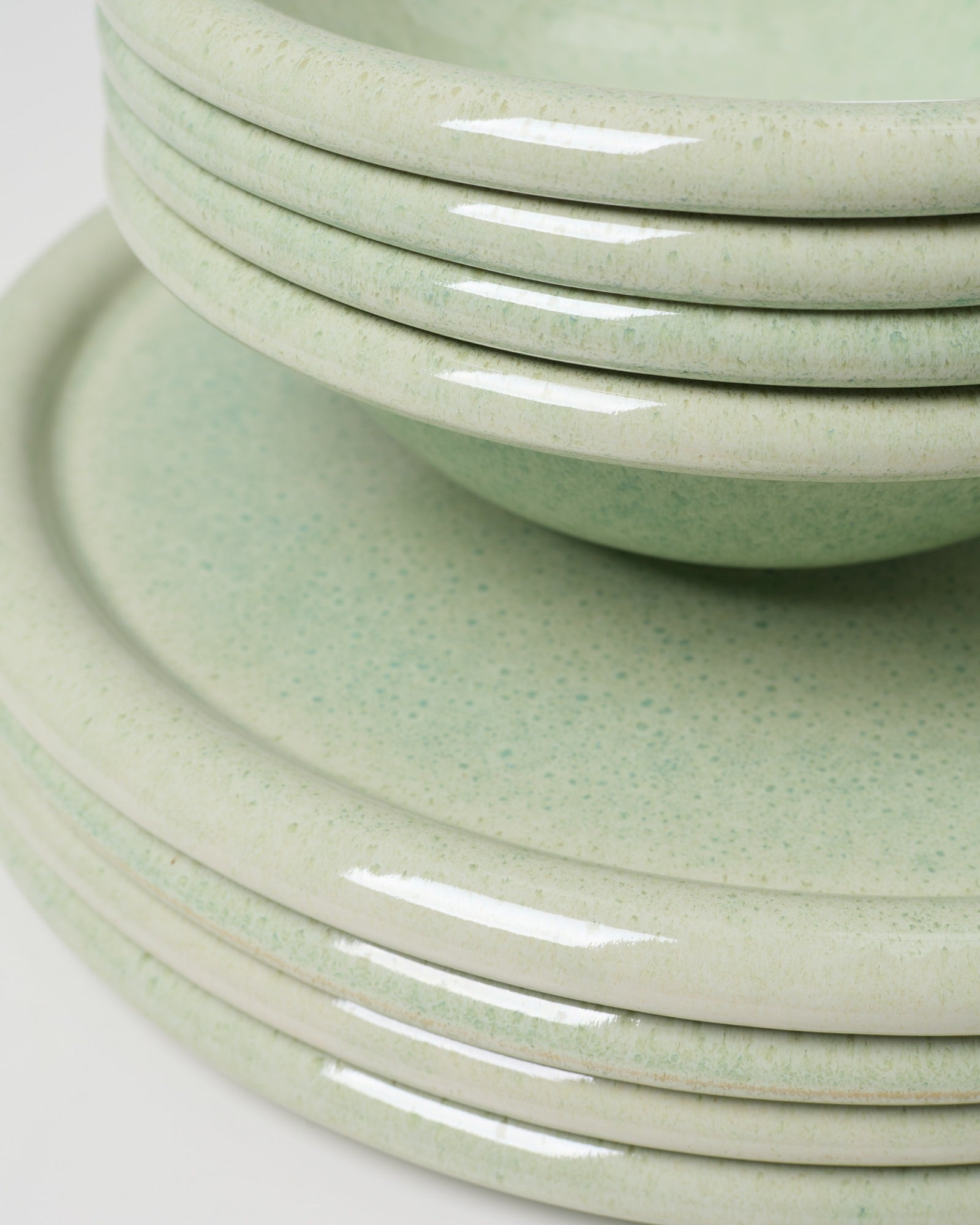 Ein Stapel glänzender, grün gesprenkelter Teller und Schalen aus Keramik.