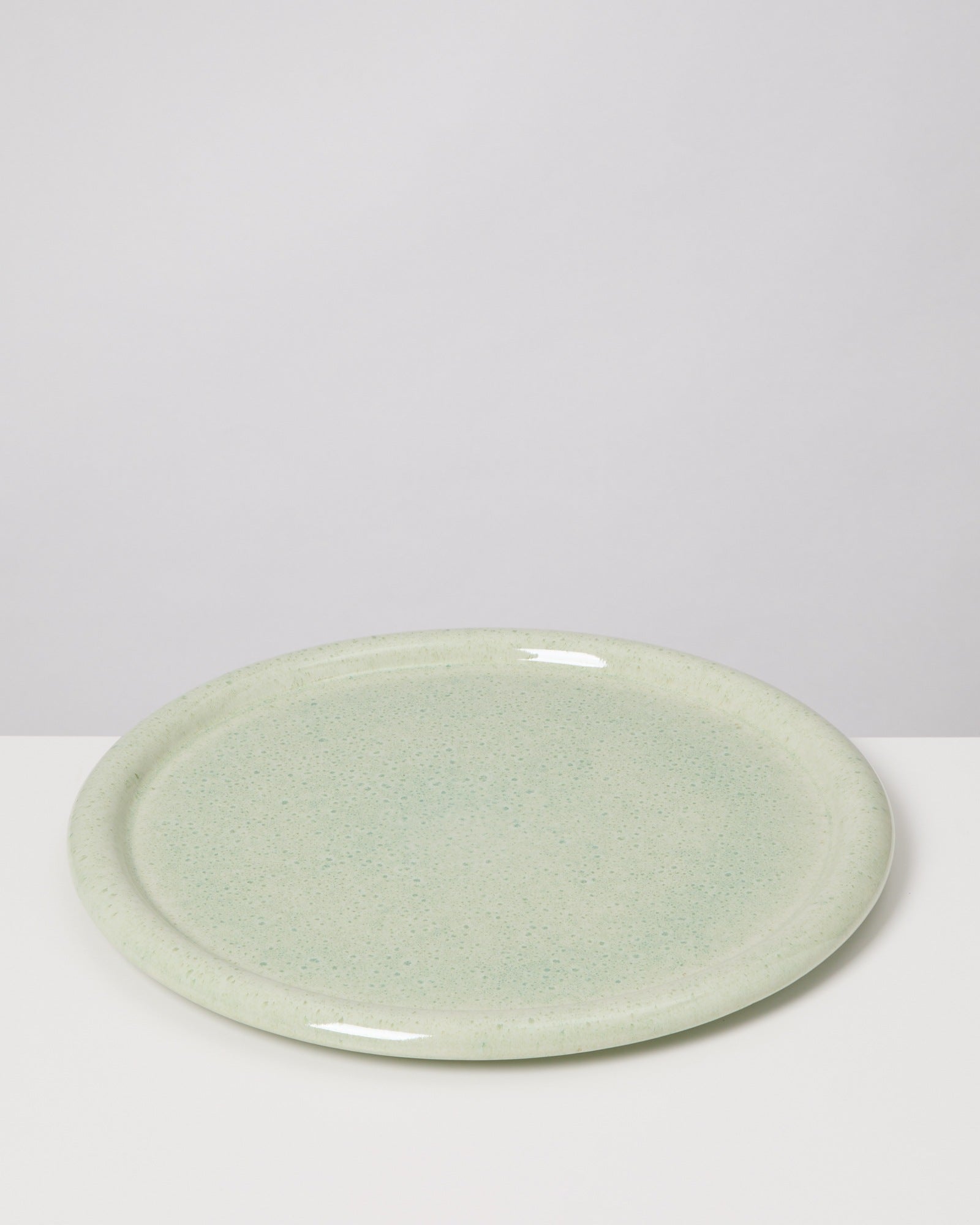 Grüner, runder Keramikteller auf weißem Hintergrund.