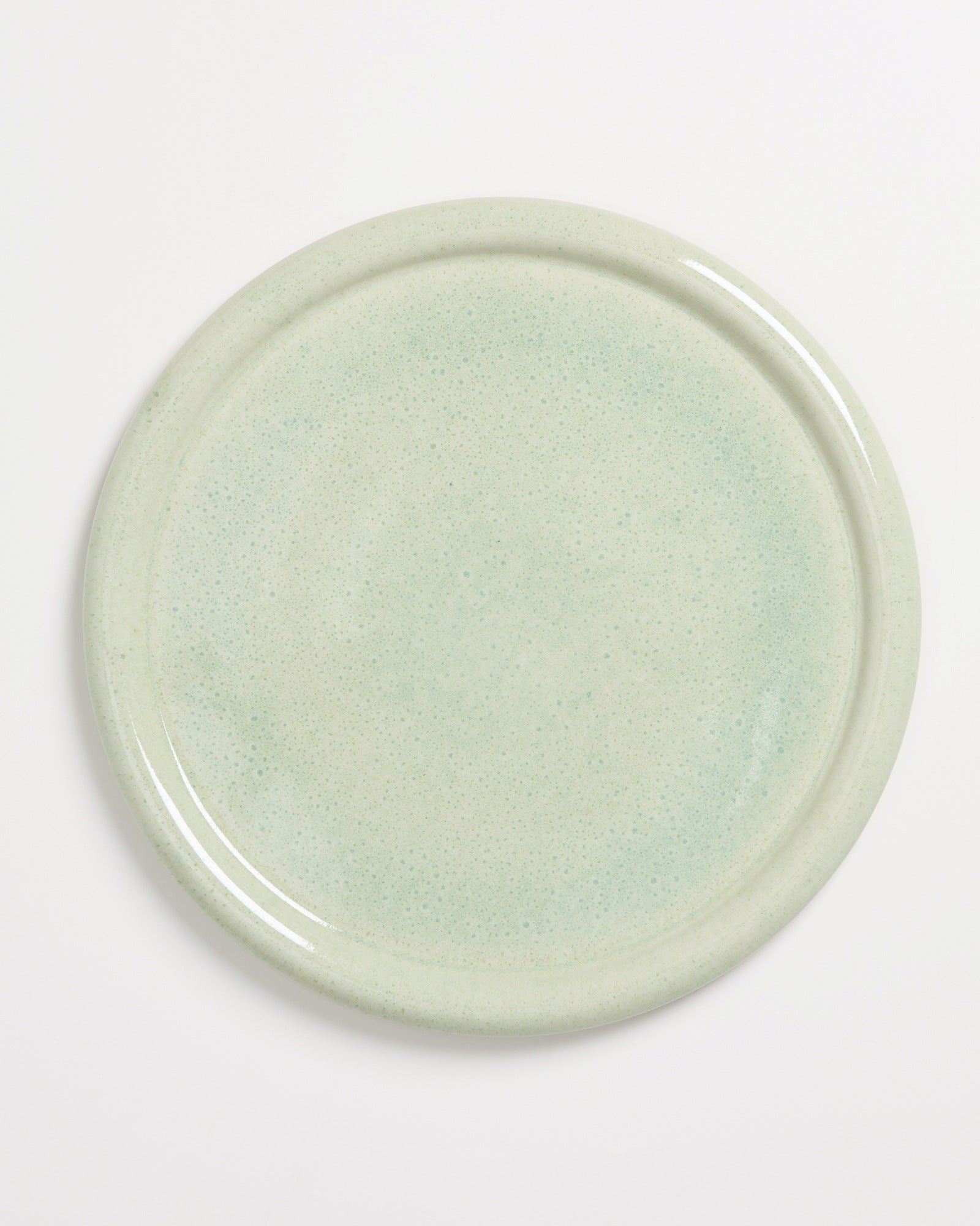 Ein runder, heller grüner Teller mit einem subtilen Sprenkelmuster auf weißem Hintergrund.