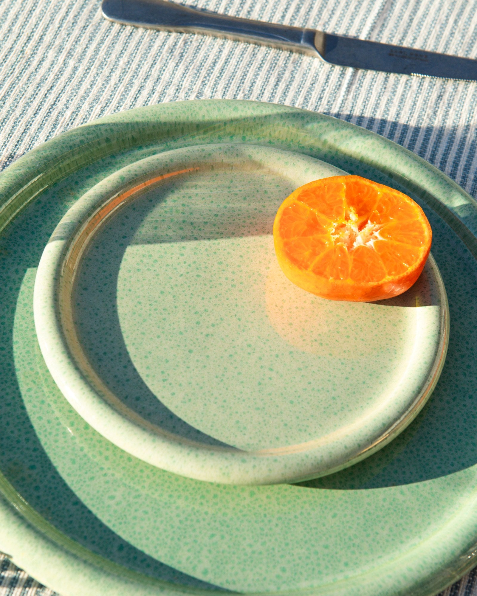 Halbe Mandarine auf zwei grünen Teller auf gestreiftem Tischtuch, mit Messer im Hintergrund.