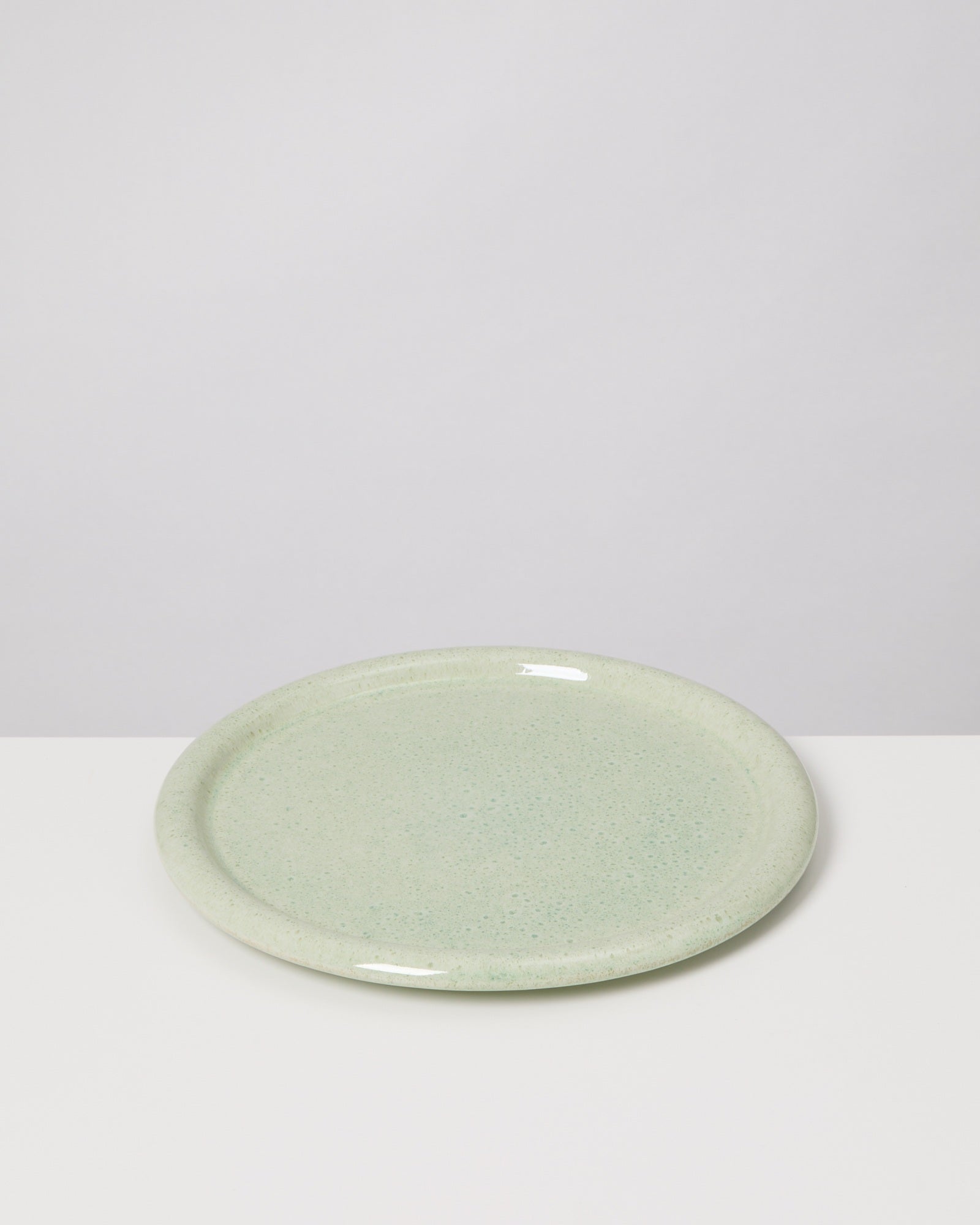 Ein runder, hellgrüner Keramikteller auf einem weißen Tisch vor einem grauen Hintergrund.