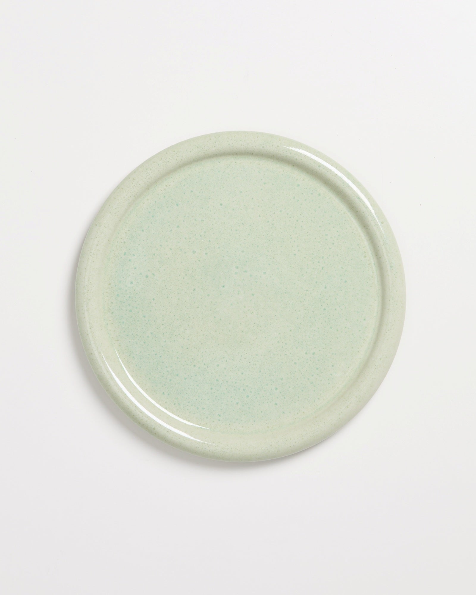 Runder, hellgrüner Keramikteller mit einer glatten, glänzenden Oberfläche auf einem weißen Hintergrund.