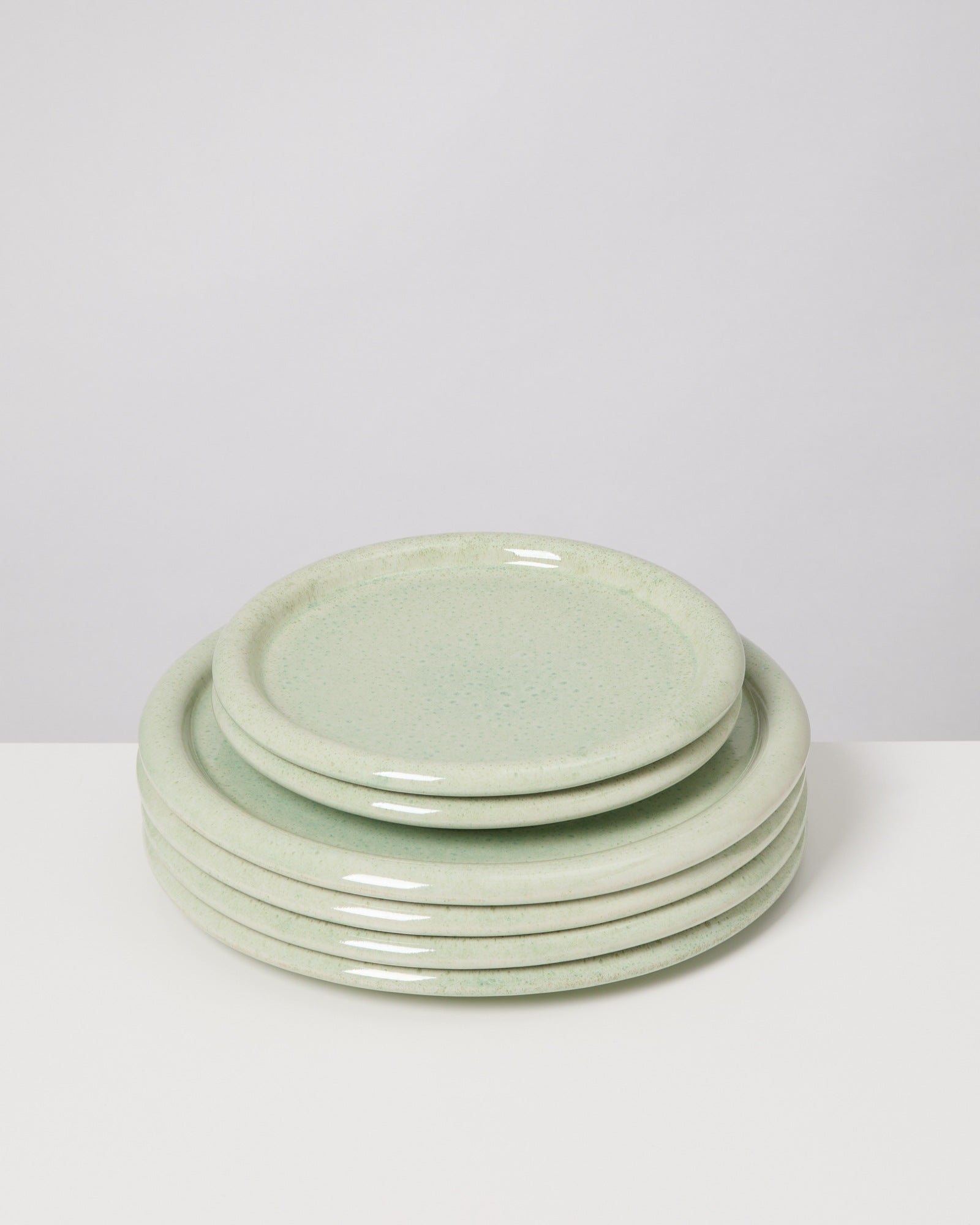 Ein Stapel aus sechs blassgrünen Tellern auf einem weißen Untergrund.