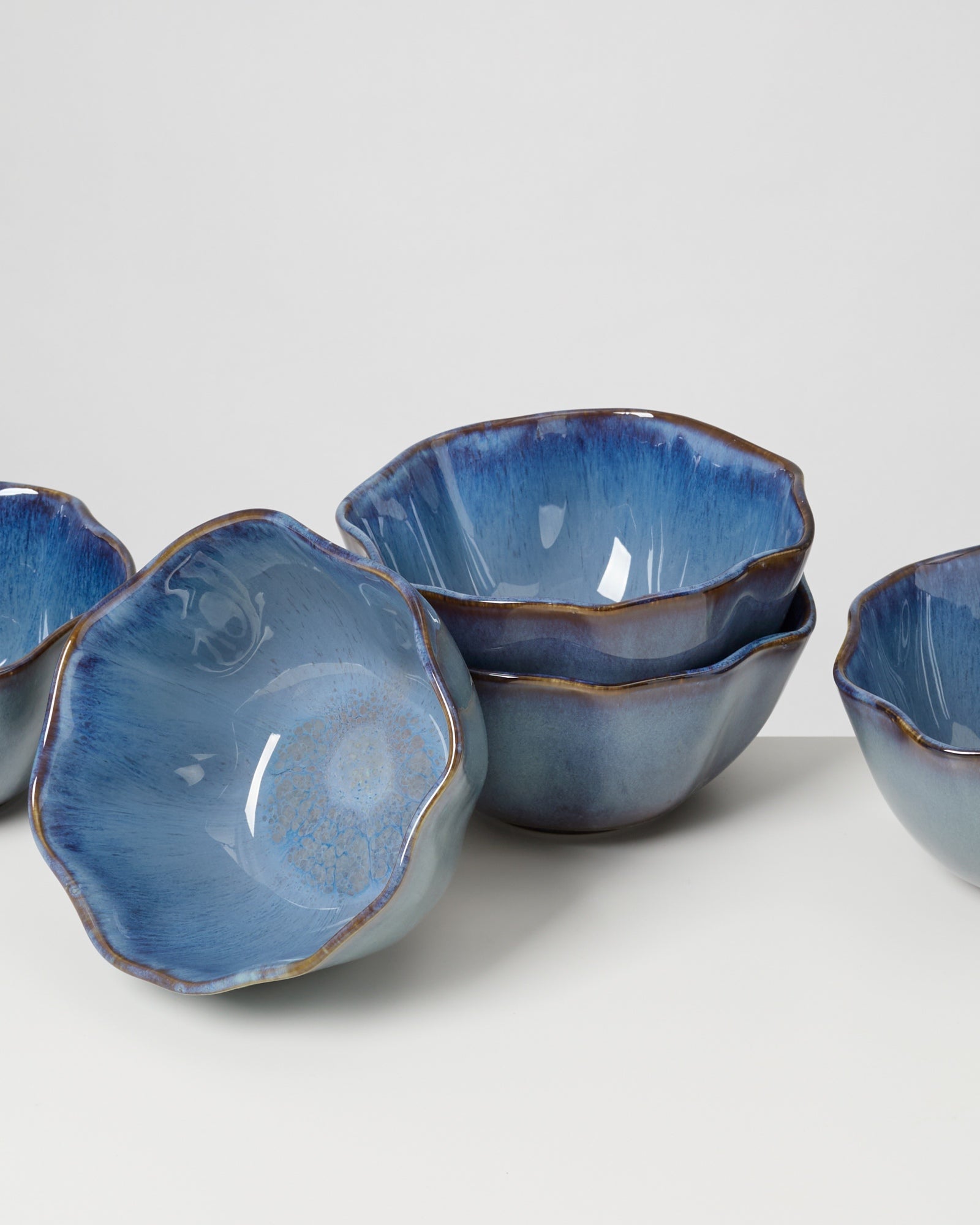 Fünf blaue Keramikschalen mit gewelltem Rand auf einer weißen Oberfläche.