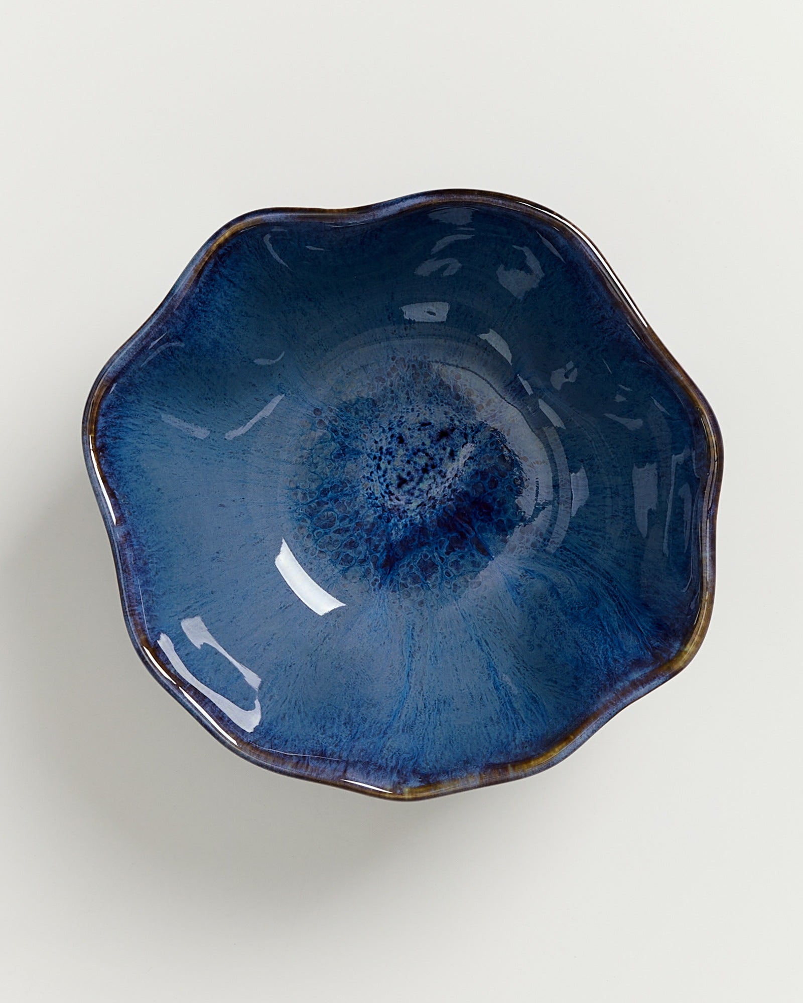 Blaue, blumenförmige Keramikschale mit glänzender Oberfläche auf weißem Hintergrund.