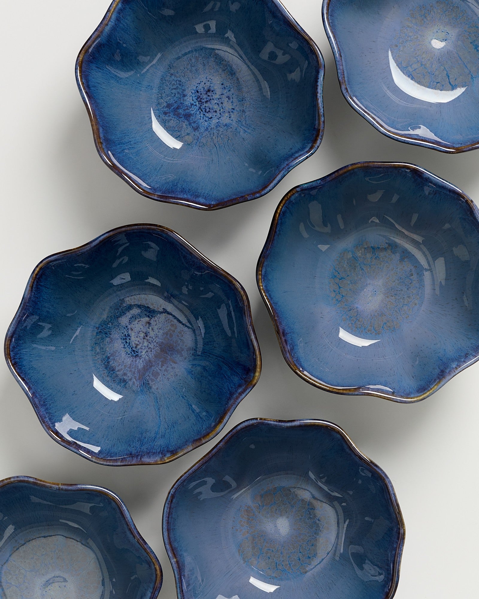 Sechs blaue, blütenförmige Schalen mit glatter Glasur und leicht unregelmäßigem Rand, auf einer weißen Oberfläche arrangiert.