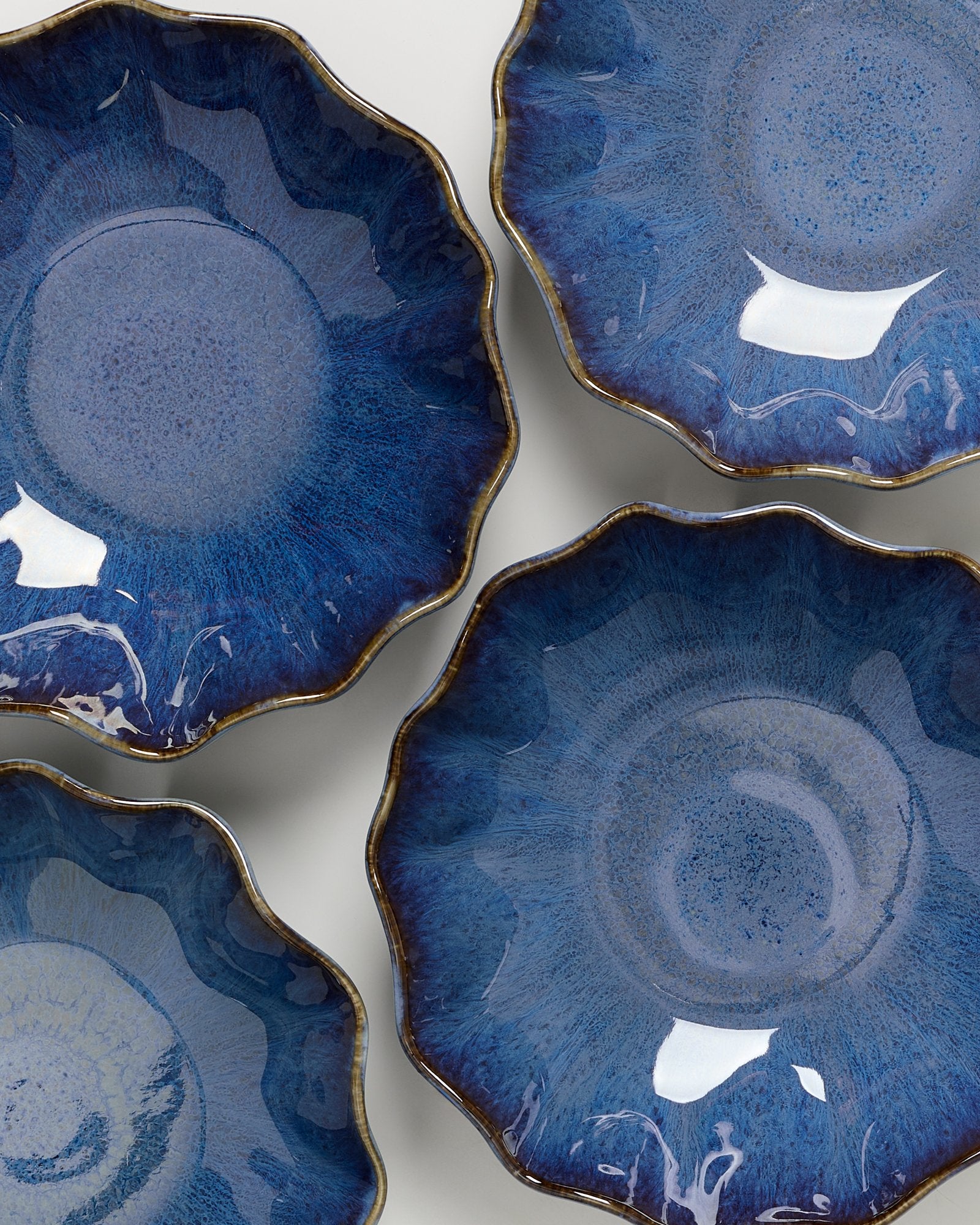 Vier dunkelblaue, muschelförmige Schalen mit gewelltem Rand und glänzender Oberfläche auf weißem Hintergrund.