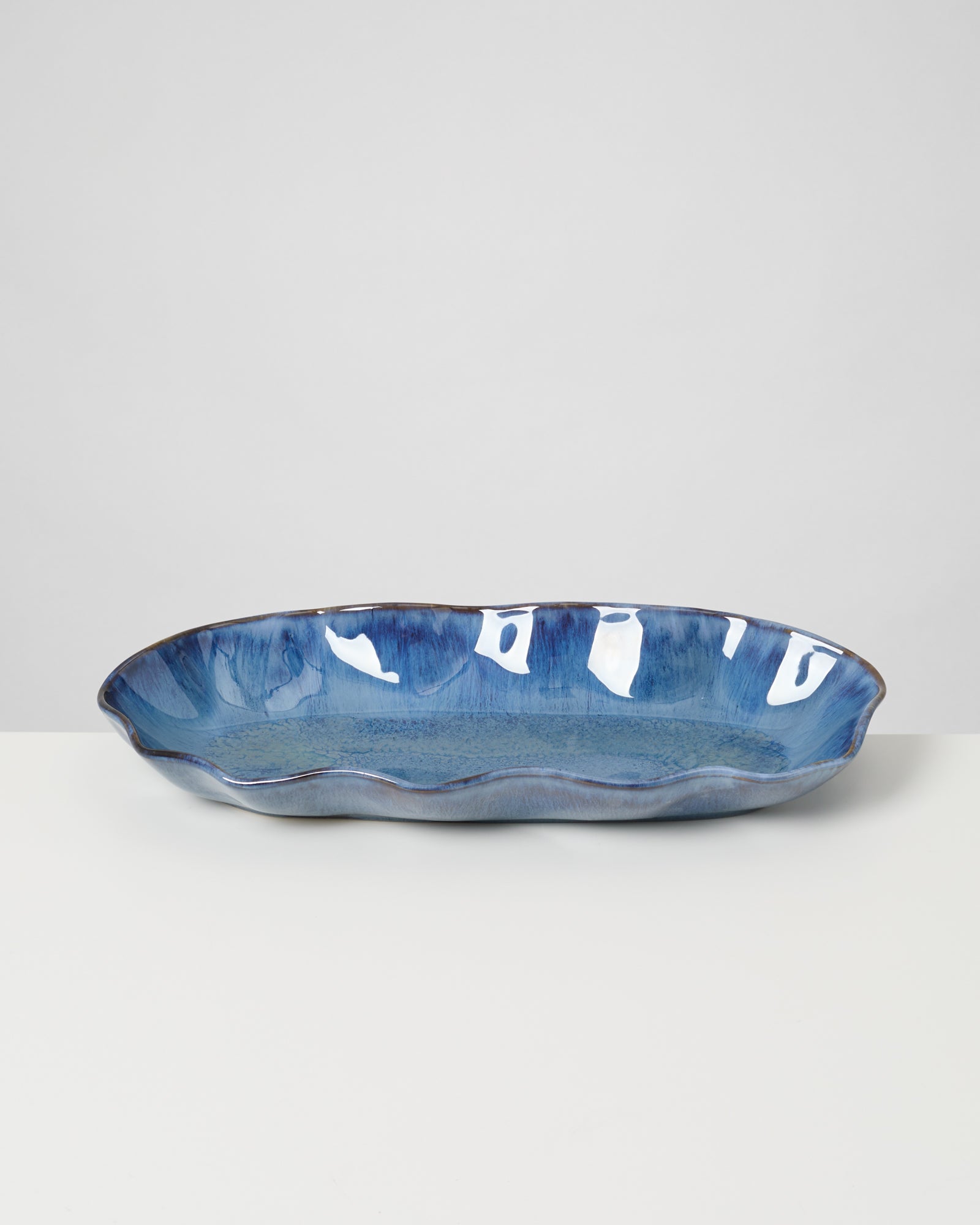 Langes, ovales, blaues Keramiktablett mit welligem Rand auf einem weißen Hintergrund.