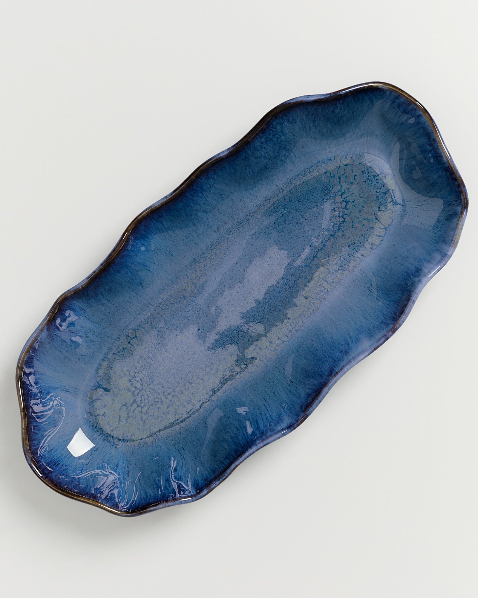 Längliche, wellenförmige blaue Keramikplatte mit glänzender Oberfläche auf weißem Hintergrund.