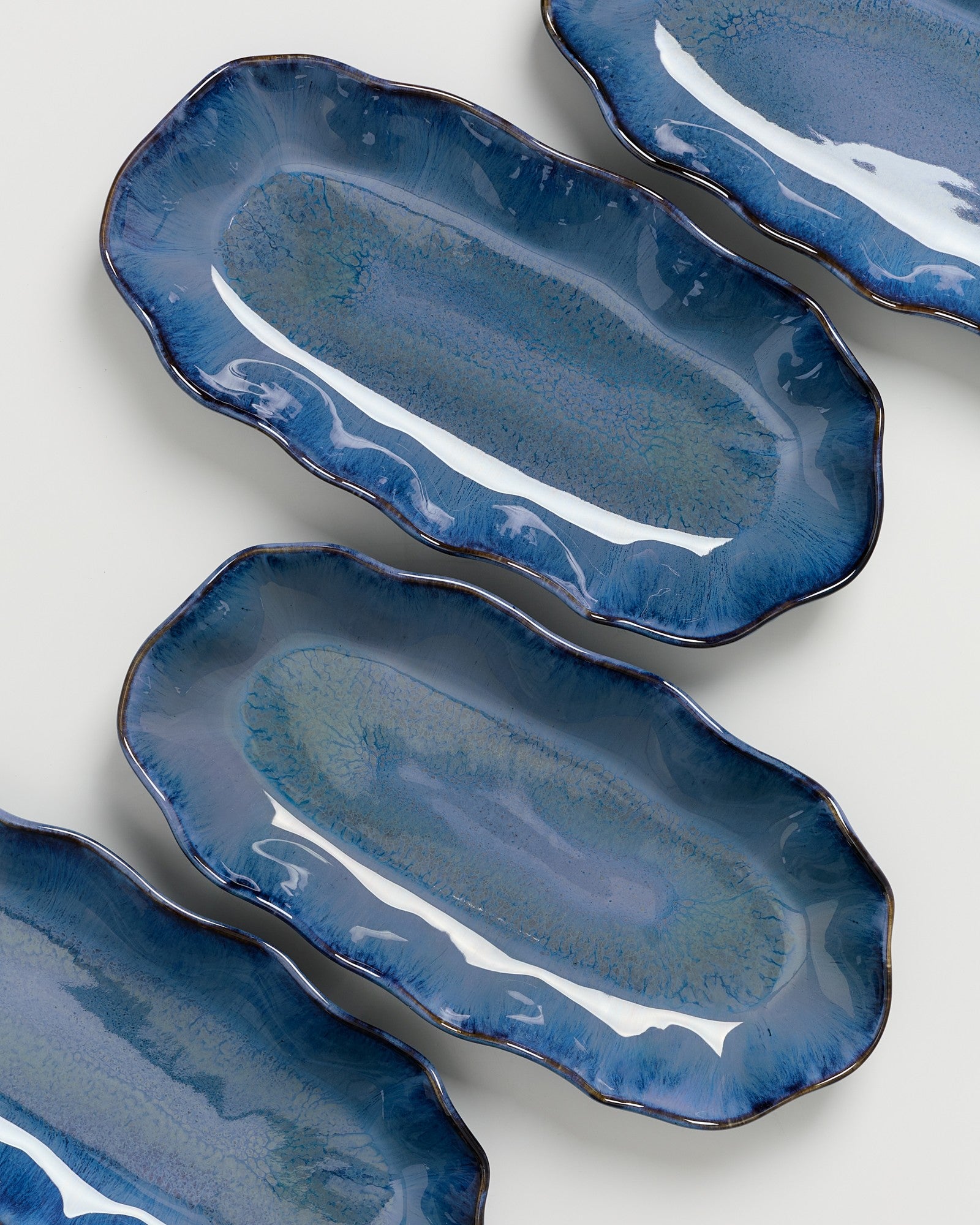 Vier blau glasierte, längliche Keramikteller mit unregelmäßiger Bogenkante auf weißem Hintergrund.