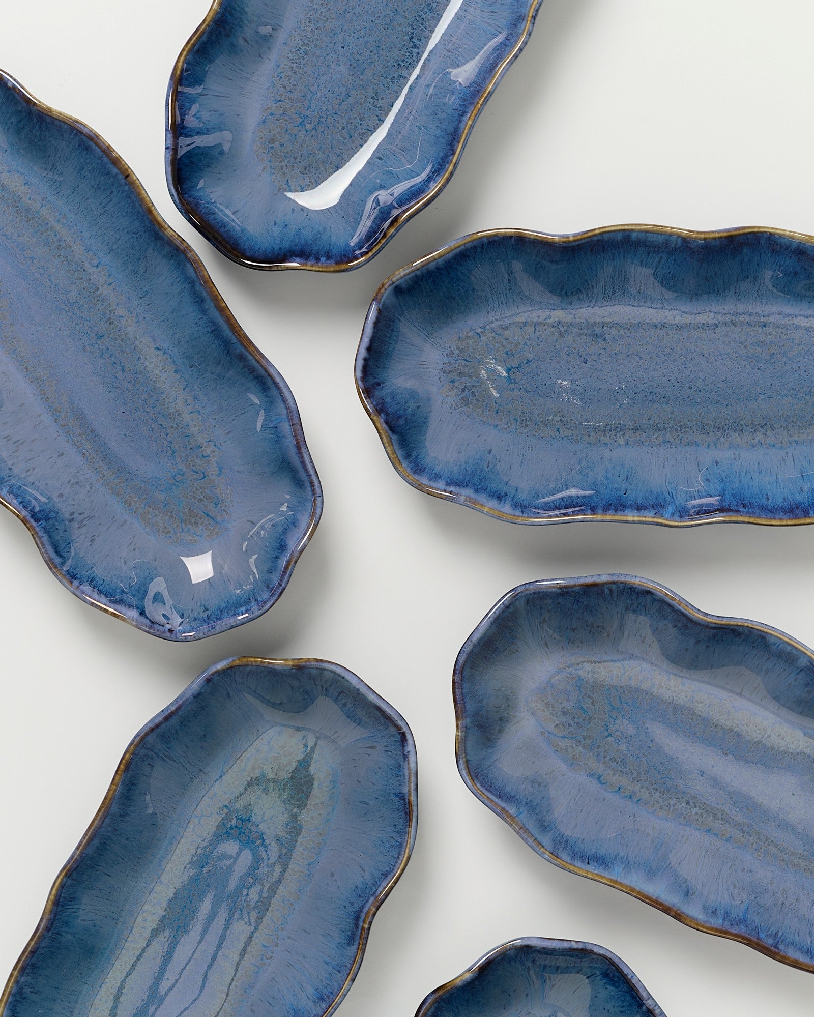 Sechs ovale Keramikteller in verschiedenen Blautönen auf einem hellen Hintergrund.