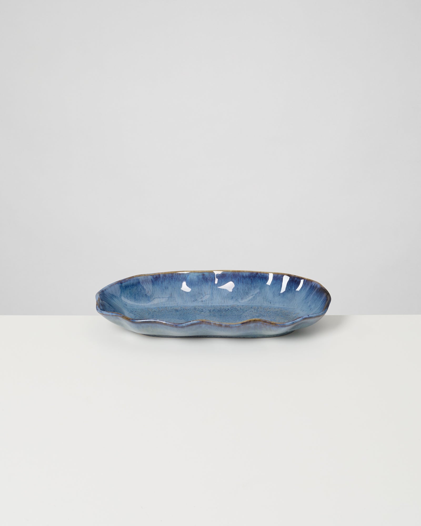 Blau glasierte, ovale Keramikschale auf einem weißen Tisch vor grauem Hintergrund.