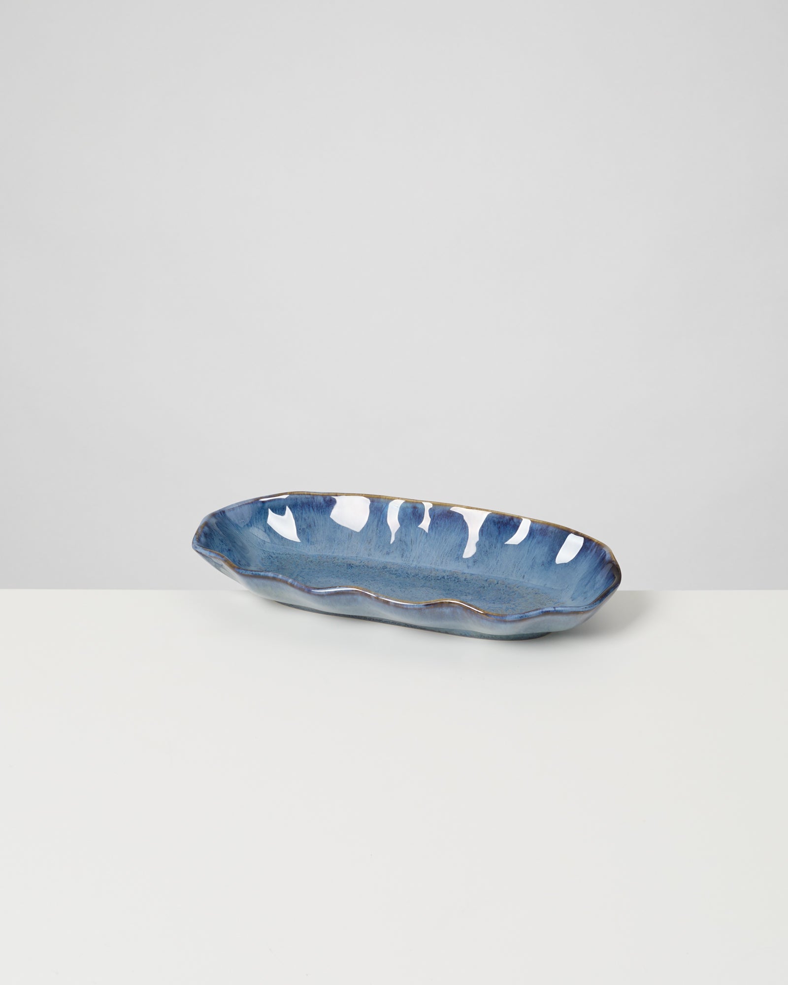 Langes, blaues Keramiktablett mit unregelmäßigem Rand auf weißem Hintergrund.