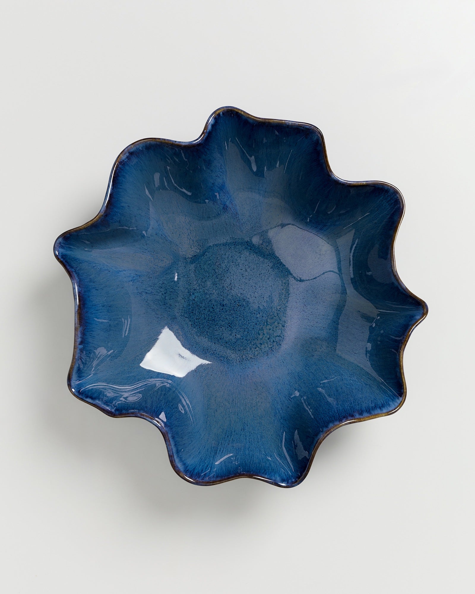 Blau glasierte, blumenförmige Keramikschale mit welligem Rand auf weißem Hintergrund.