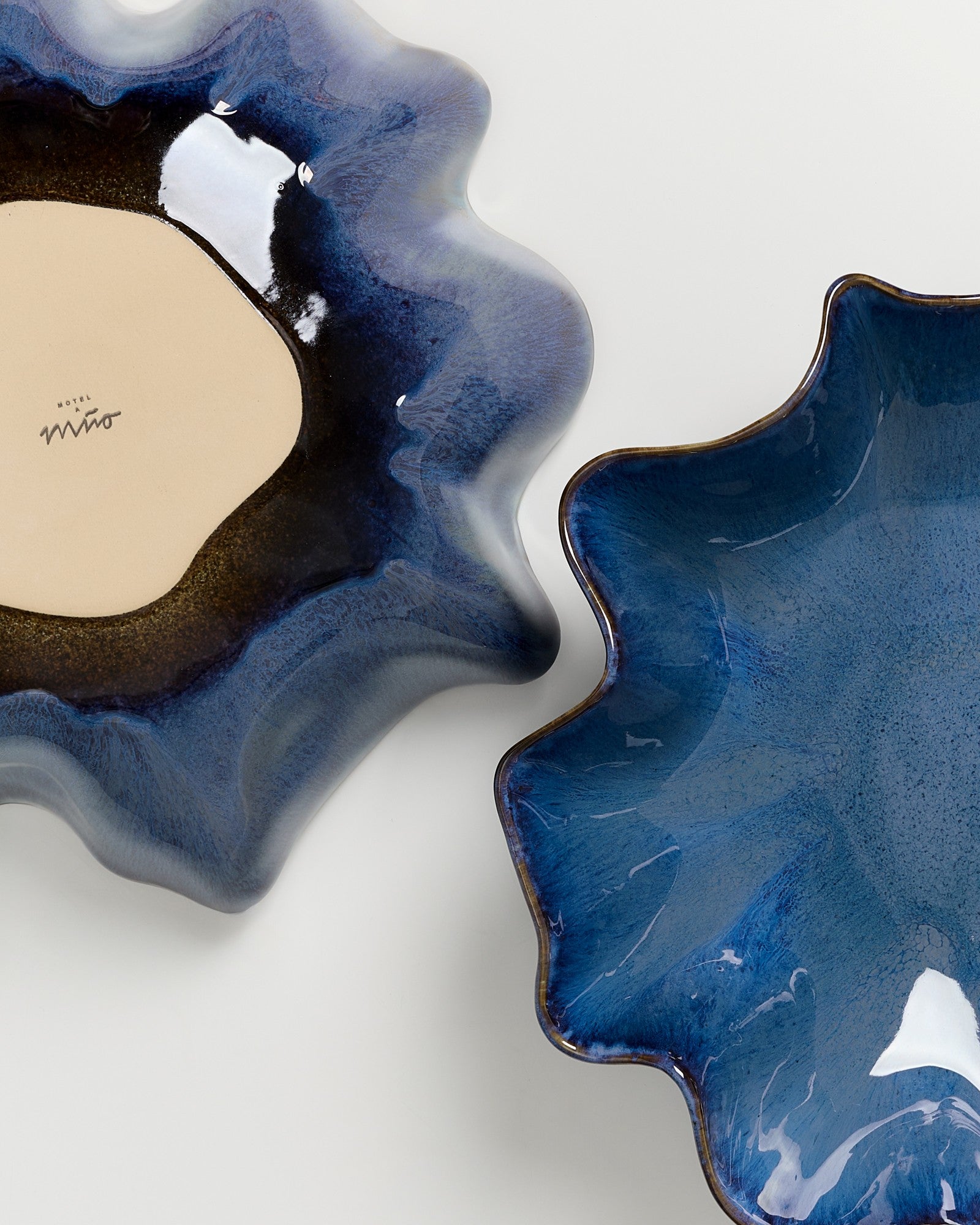 Zwei blaufarbene, wellenförmige Keramikschalen auf einer hellen Oberfläche.