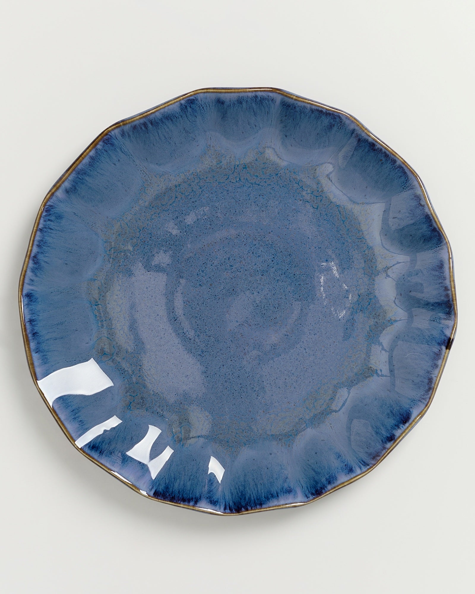 Runde, blaue Keramikplatte mit welligem Rand, Glanz und eingearbeitetem Muster auf hellem Hintergrund.