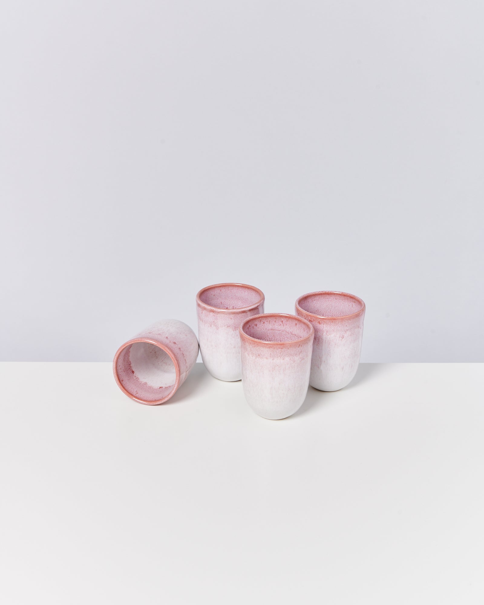 Vier weiße Keramikbecher mit rosa Rand auf weißem Hintergrund, einer liegt seitlich.