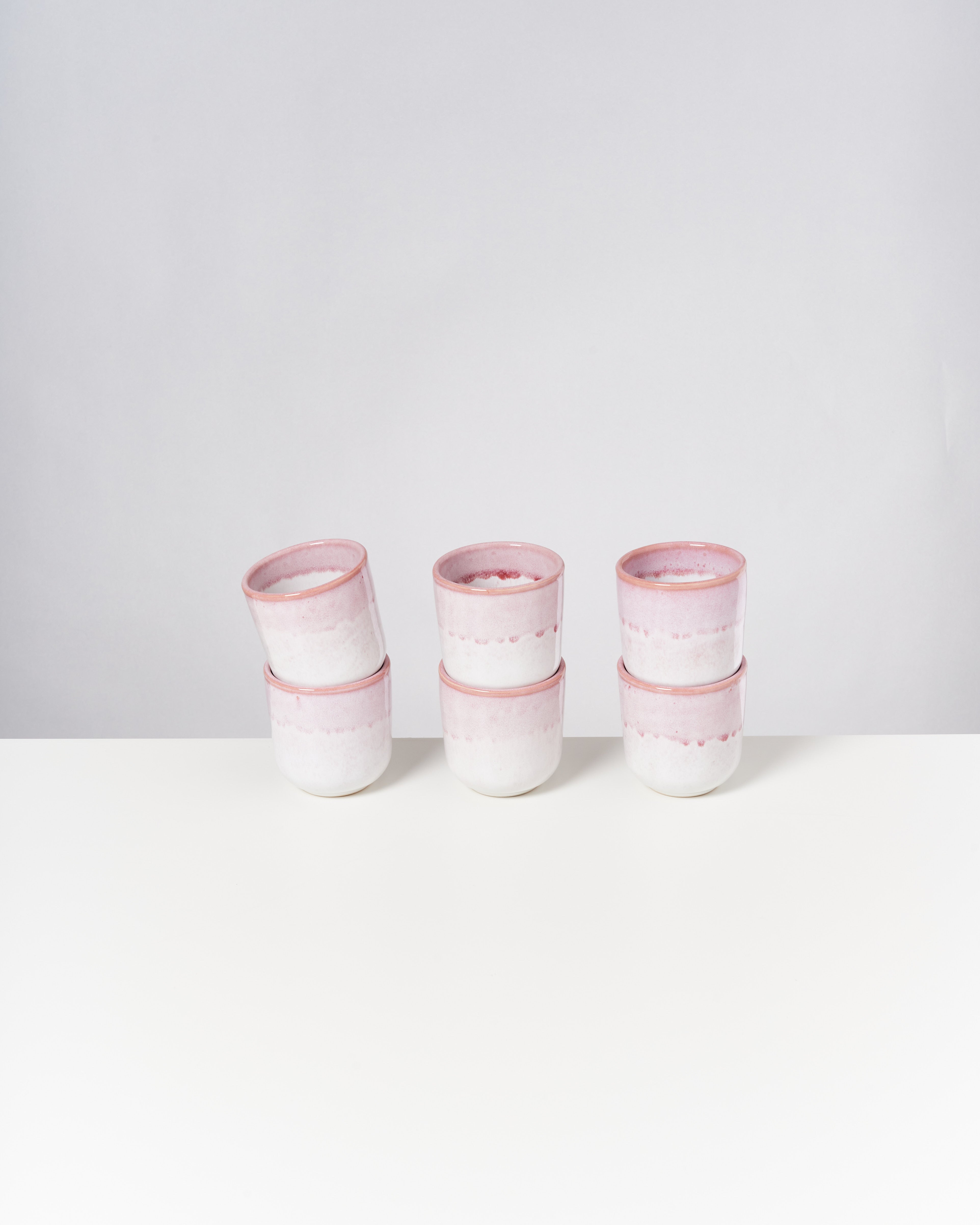 Sechs rosa-weiße Keramiktöpfe in zwei Stapeln auf einem weißen Tisch vor grauem Hintergrund.