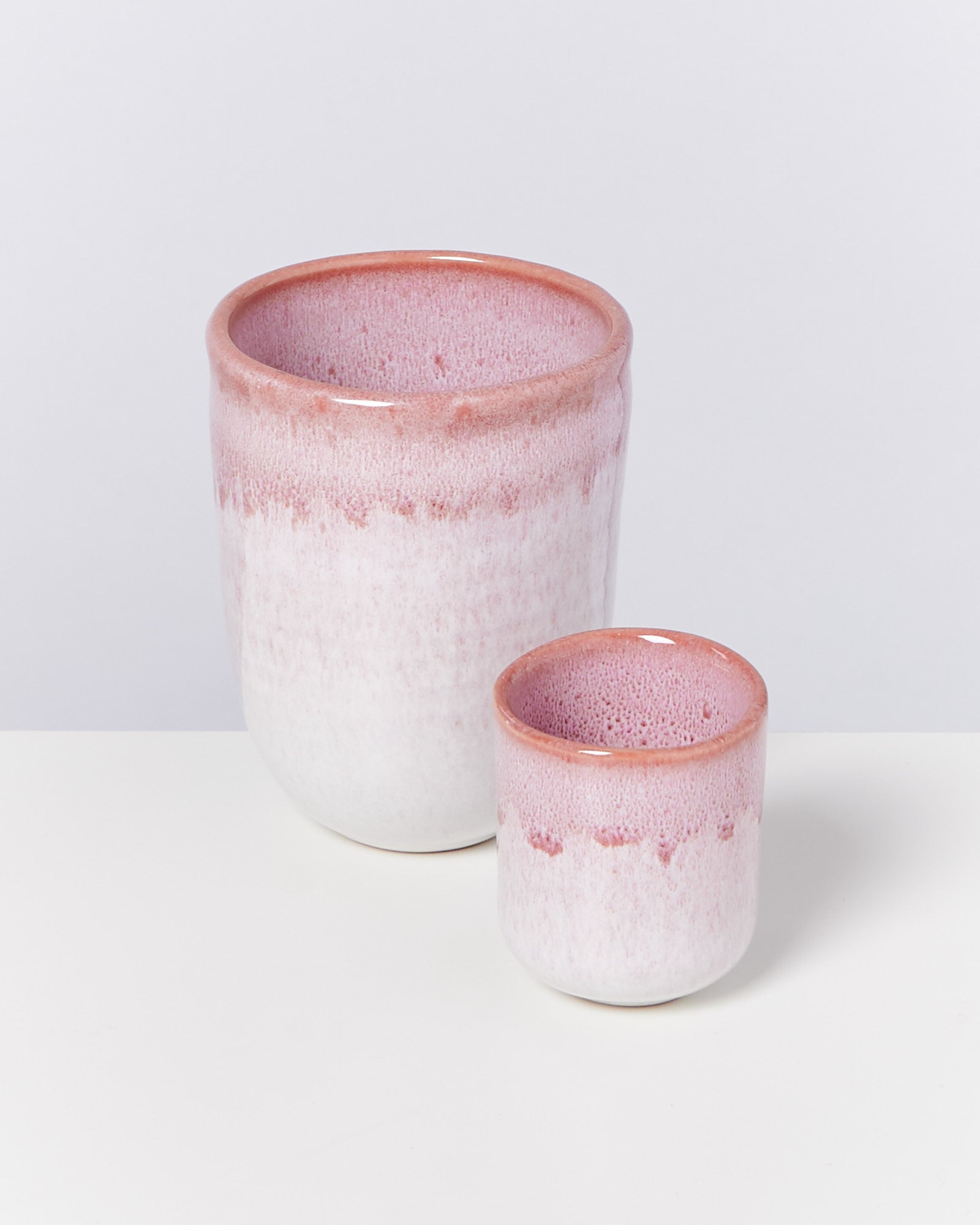 Zwei rosa-weiße Keramiktöpfe stehen auf einer weißen Oberfläche vor einem grauen Hintergrund.