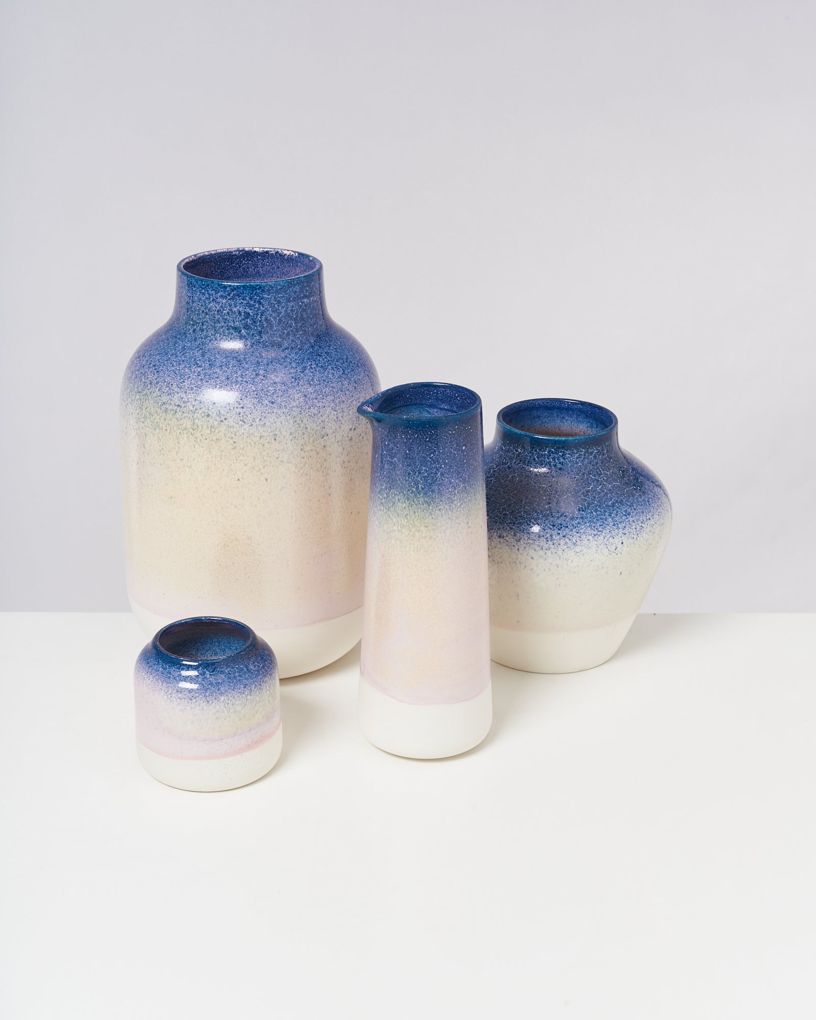 Vier keramische Gefäße mit blau-beigem Farbverlauf stehen auf einem weißen Untergrund.