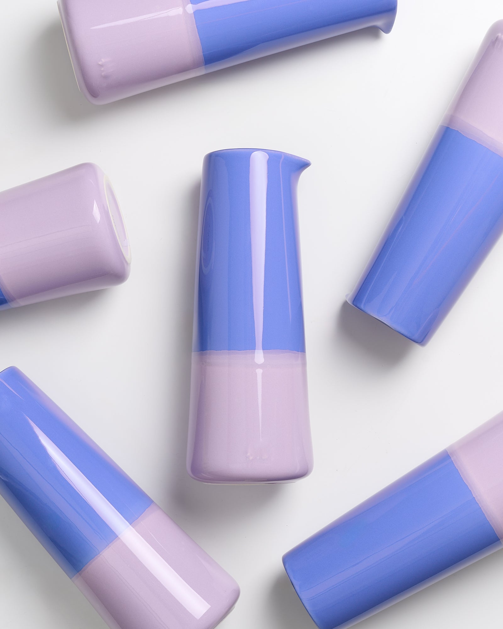 Sechs pastellfarbene, zweifarbige Vasen in Lila und Blau auf einem weißen Hintergrund arrangiert.