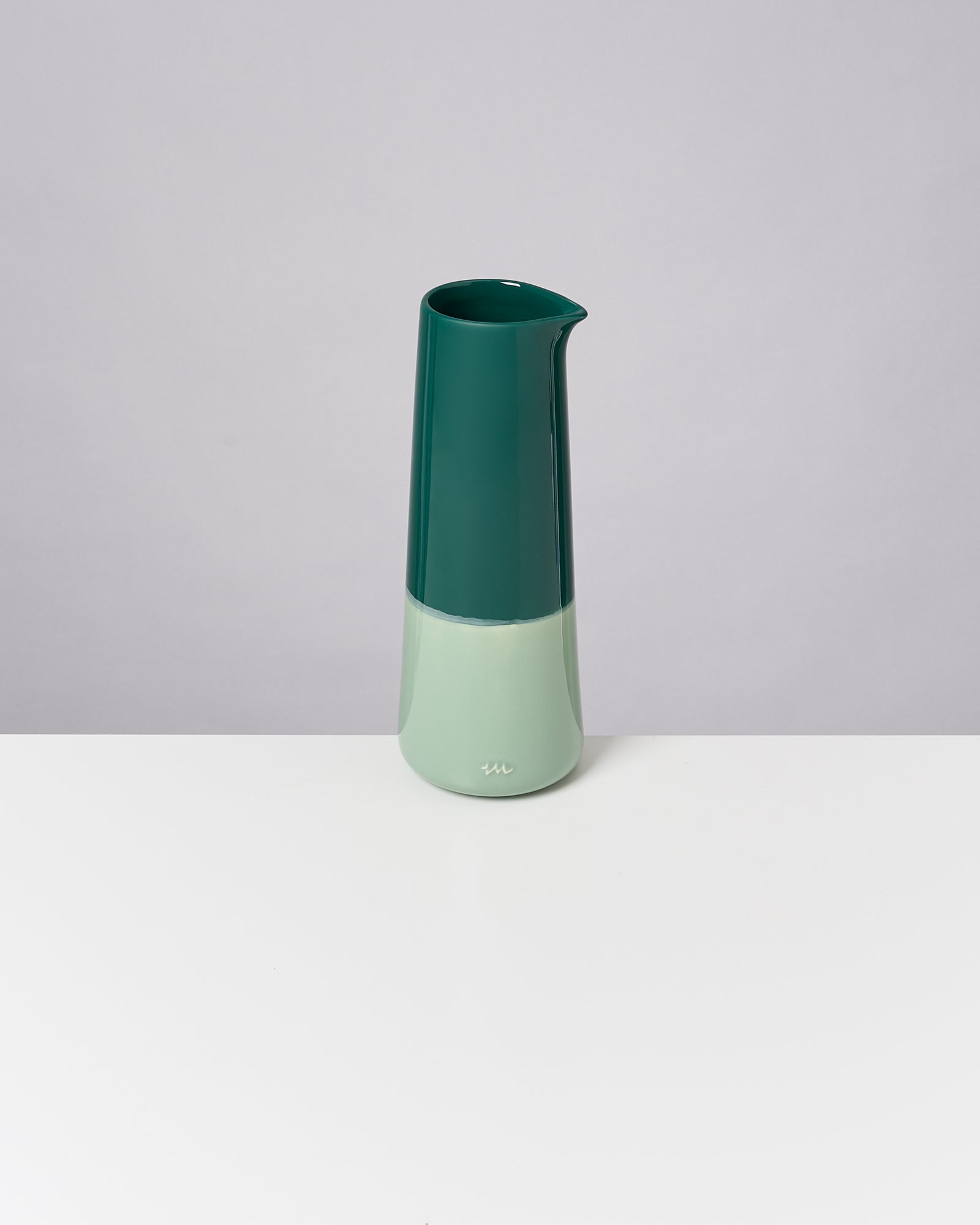 Grüne Karaffe im minimalistischen Design steht auf einem weißen Tisch vor grauem Hintergrund.