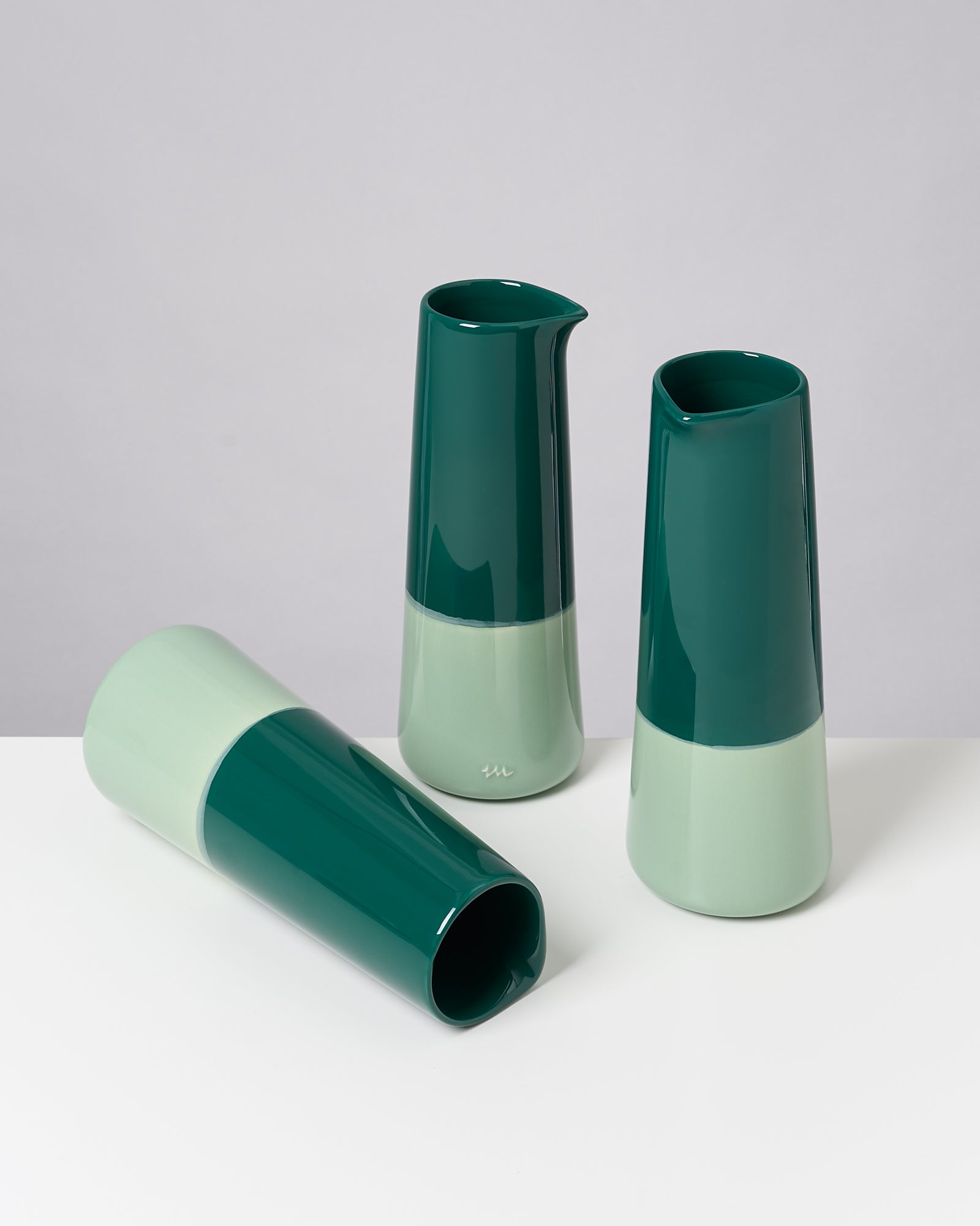 Drei zweifarbige Karaffen in grün und mint stehen auf einer weißen Oberfläche, eine liegt quer.